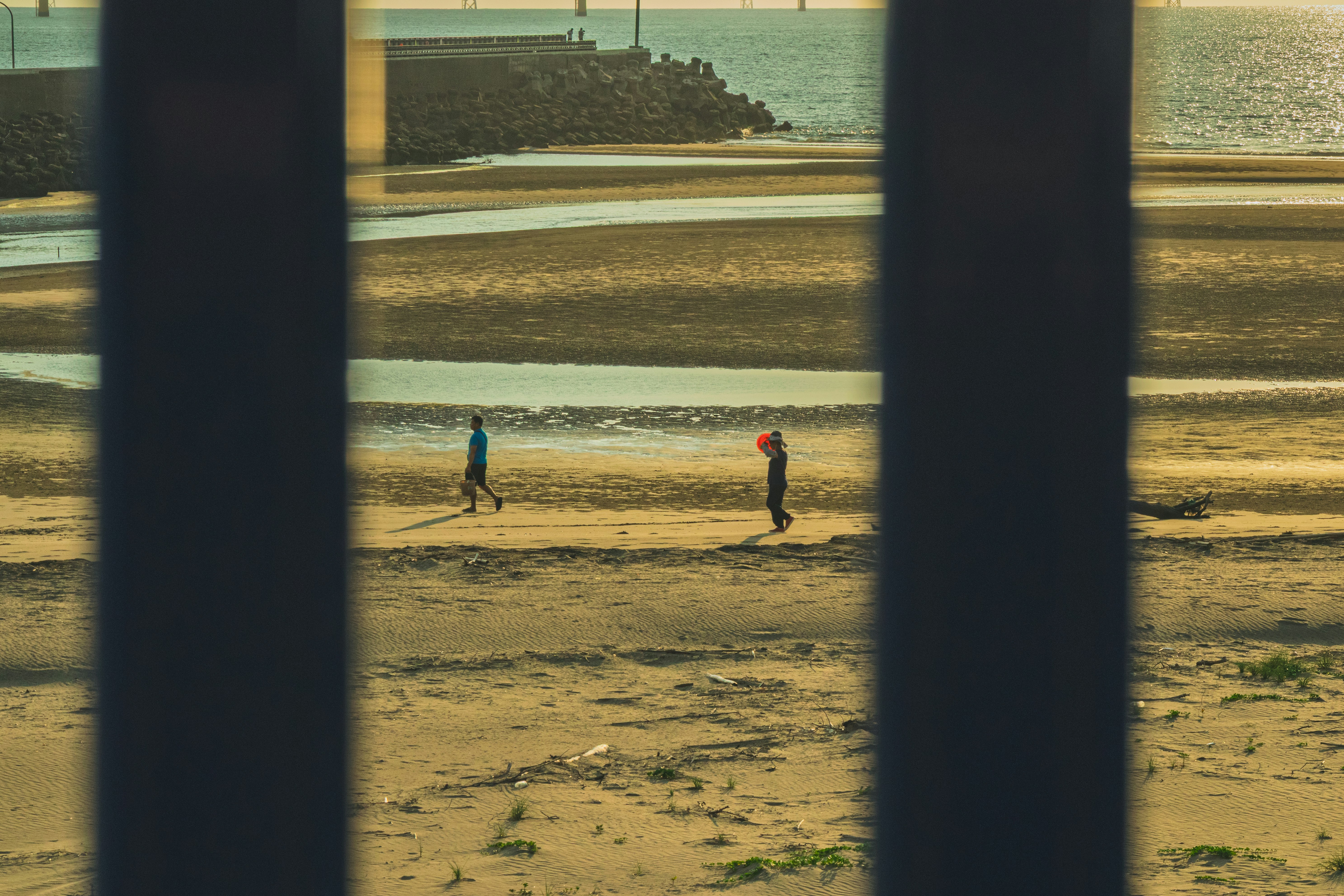 Paseo en la playa visto entre columnas de un muelle