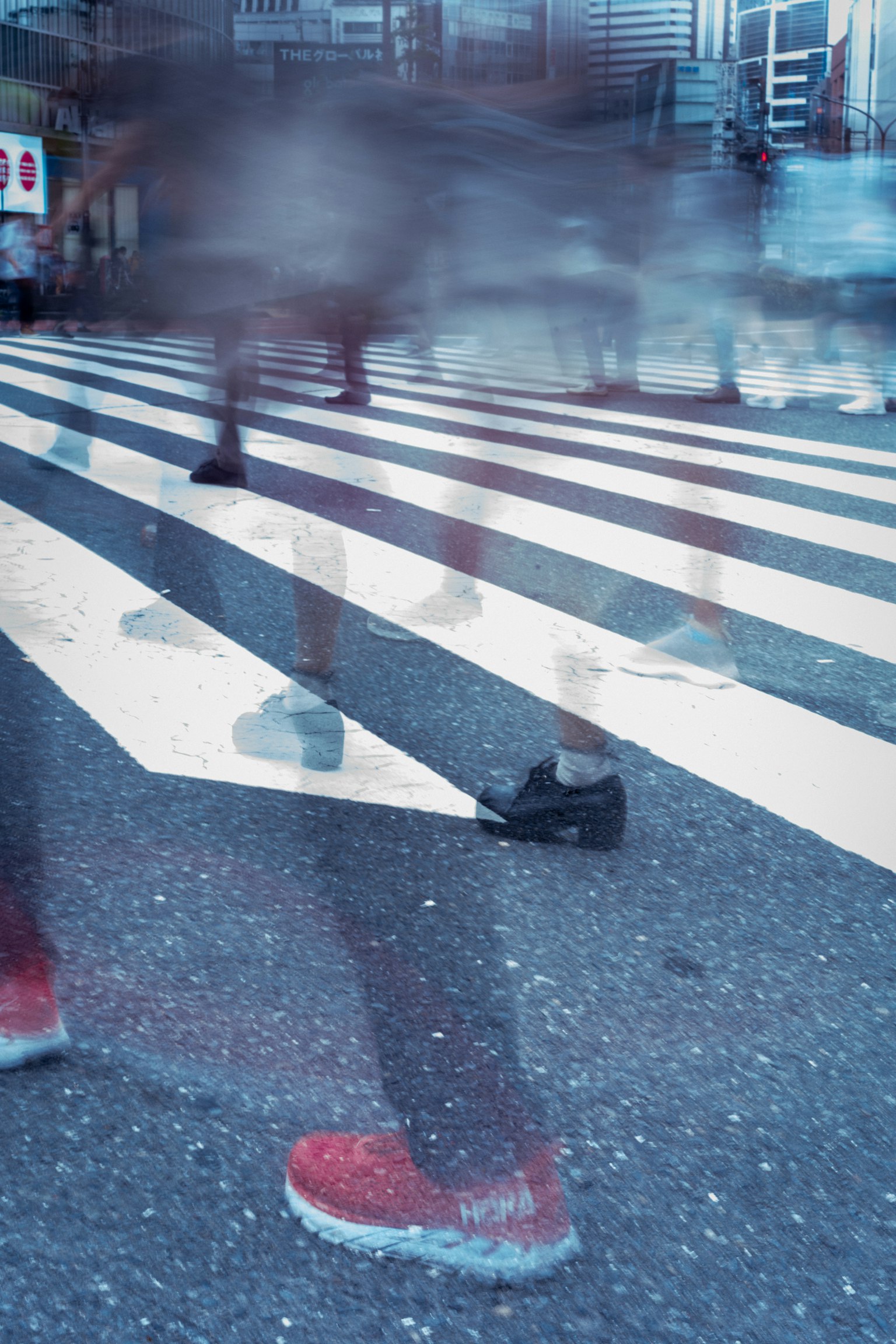 Immagine sfocata di persone che attraversano una strada con scarpe rosse e nere in evidenza