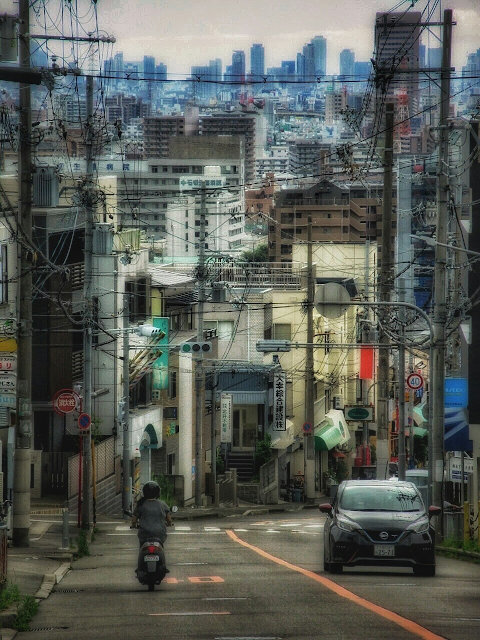 Jalan menurun di Tokyo dengan mobil dan sepeda motor melintas di latar belakang gedung-gedung tinggi