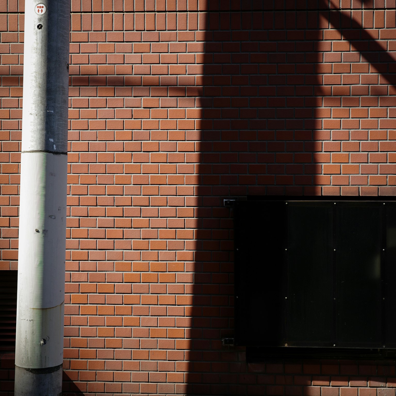Schatten auf einer Ziegelwand mit einem Pfosten und einem dunklen Panel