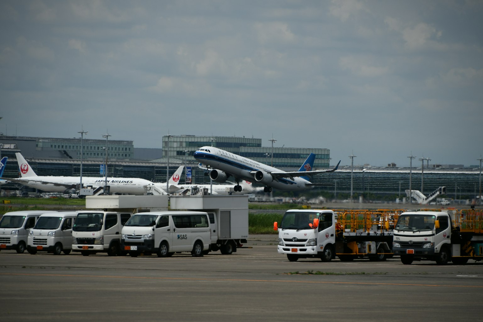 เครื่องบินขึ้นจากรันเวย์สนามบินพร้อมกับรถบรรทุกจอดอยู่