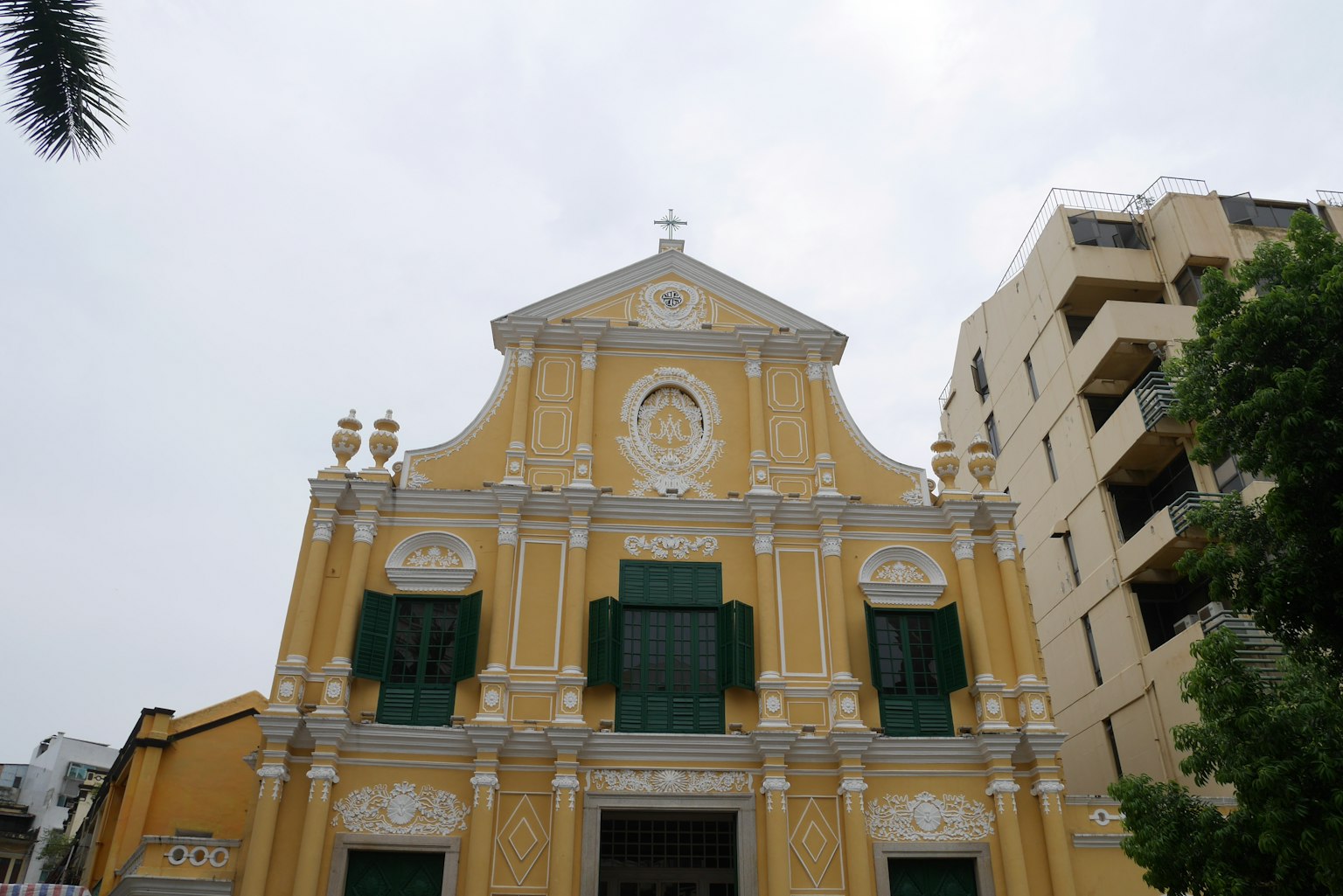 Fassade einer historischen Kirche mit gelbem Äußeren und grünen Fenstern mit aufwendigen Verzierungen