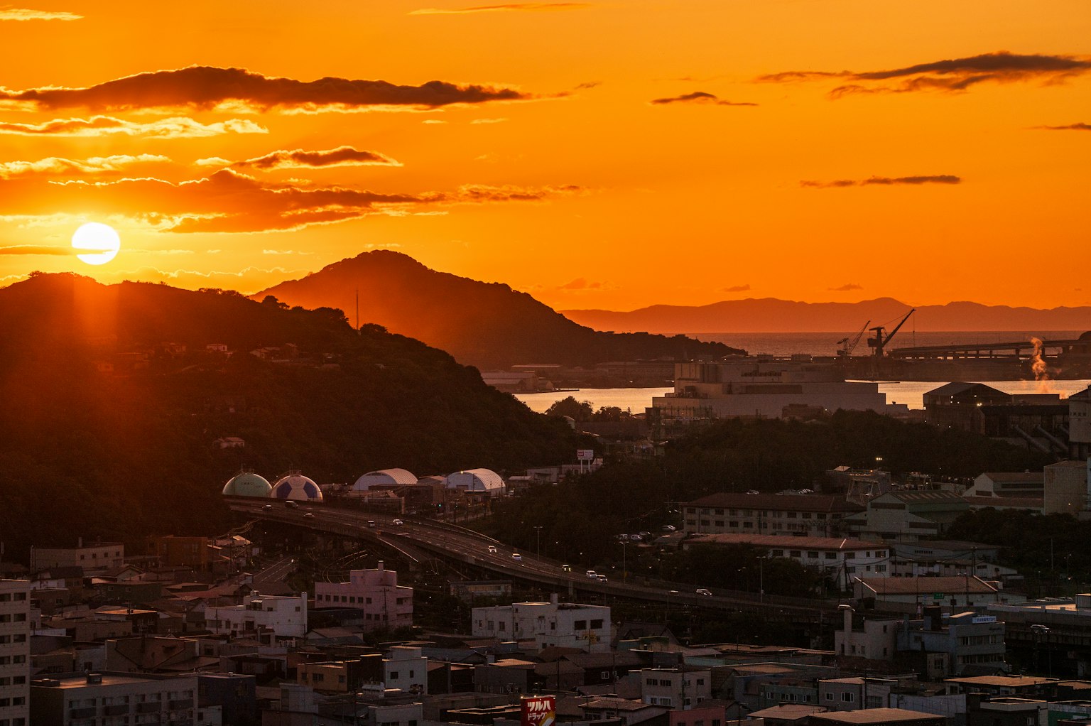 日落時的城市風景，太陽在山丘和水域後面落下