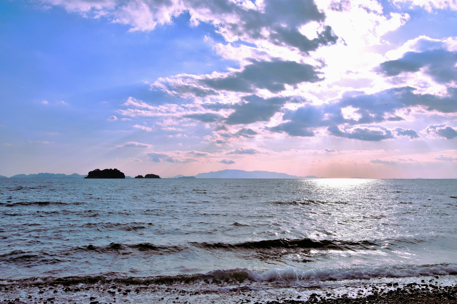 Malerscher Blick auf das Meer und die Inseln unter einem bewölkten Himmel mit Sonnenlicht, das sich auf dem Wasser spiegelt