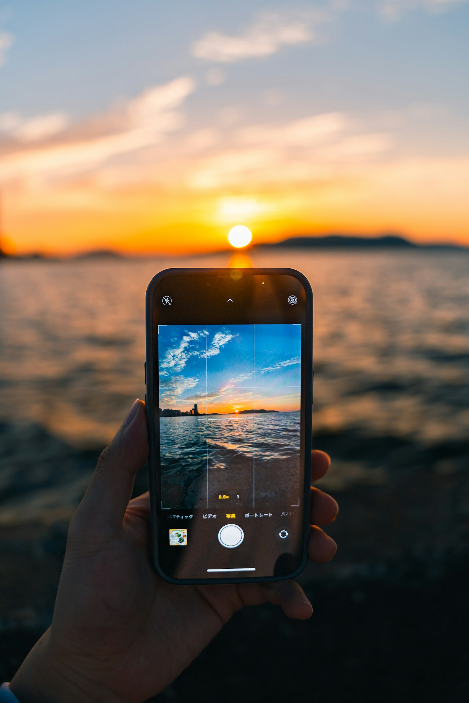 Mano che tiene uno smartphone che cattura un tramonto sull'oceano