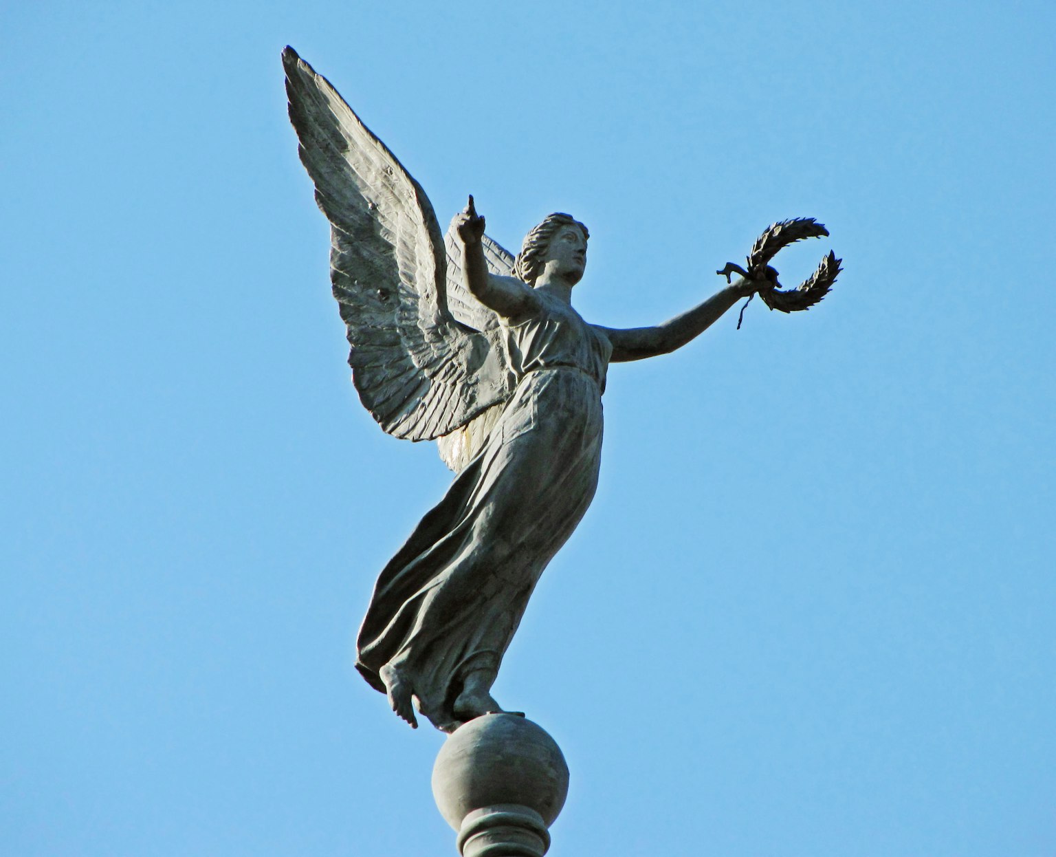Una estatua de bronce de un ángel sosteniendo una corona contra un cielo azul