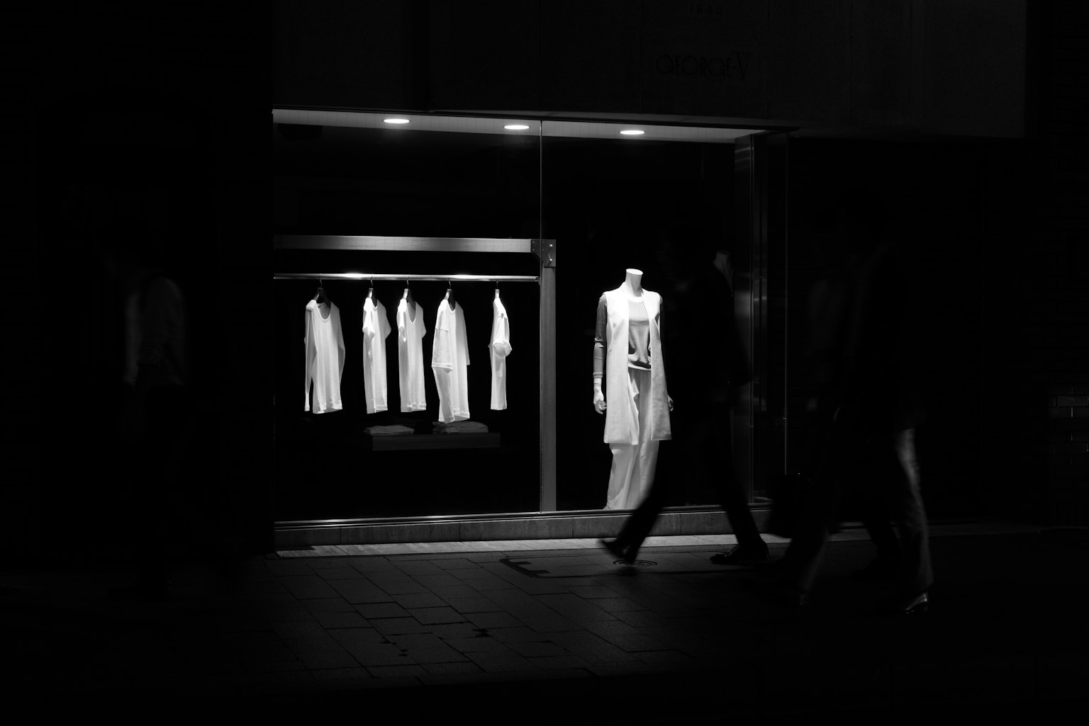 黑暗背景中展示白色衣物的商店櫥窗和路人