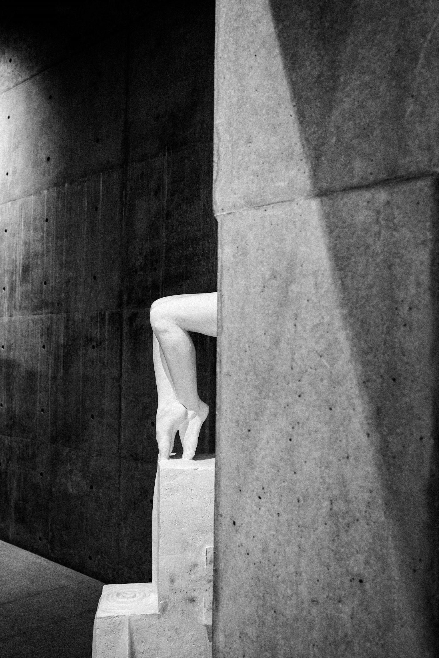 A white leg in high heels partially visible behind a concrete wall