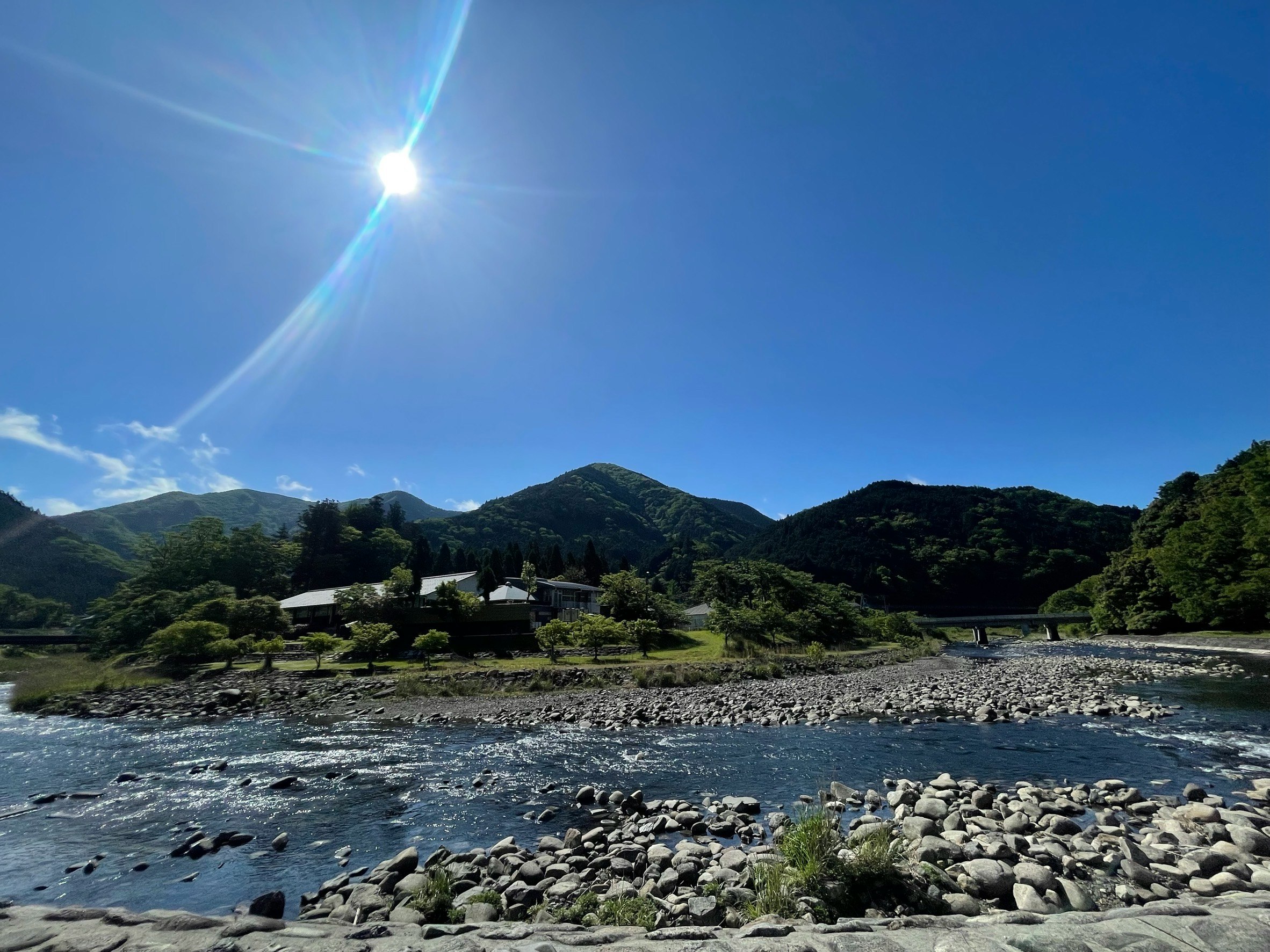 川沿いの石が並ぶ河原と山並み、快晴の青空