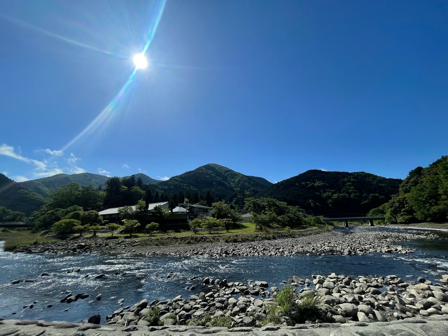 Pemandangan sungai dan pegunungan di bawah langit biru cerah dengan matahari bersinar