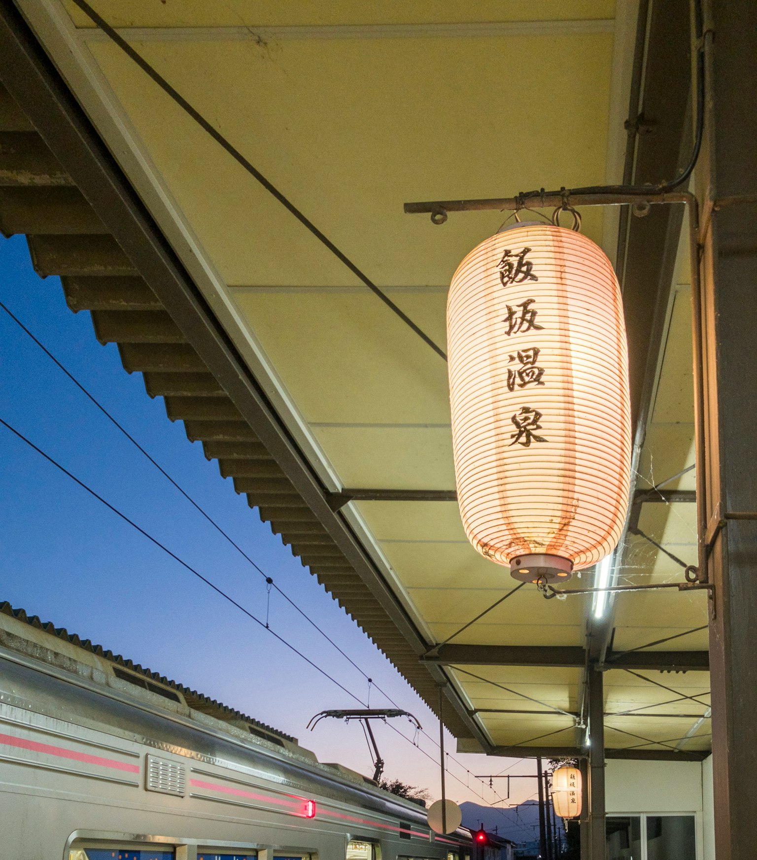 โคมไฟแขวนใต้หลังคาสถานีรถไฟและรถไฟในพื้นหลัง