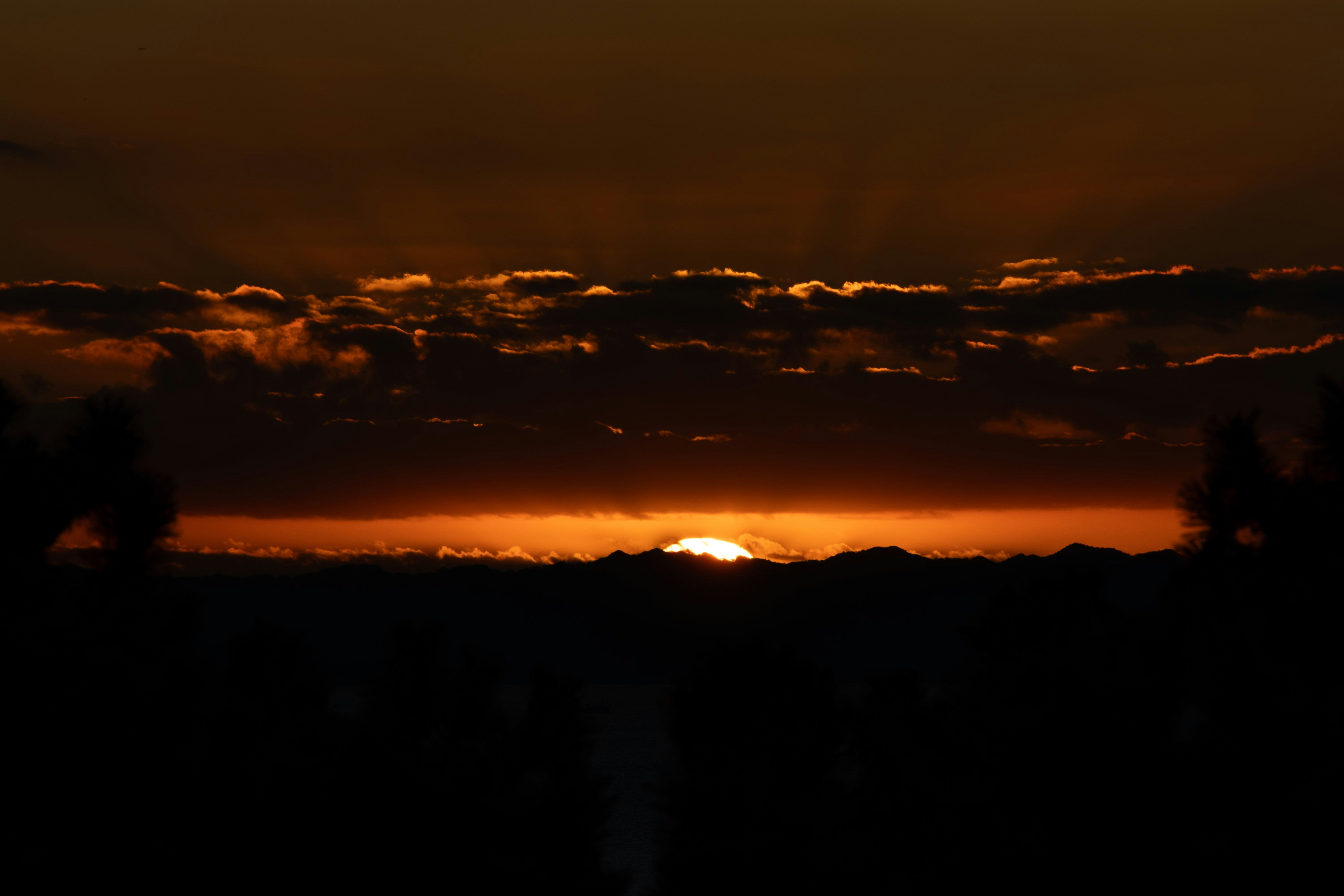 夕焼けの雲間から差し込む光のある山のシルエット