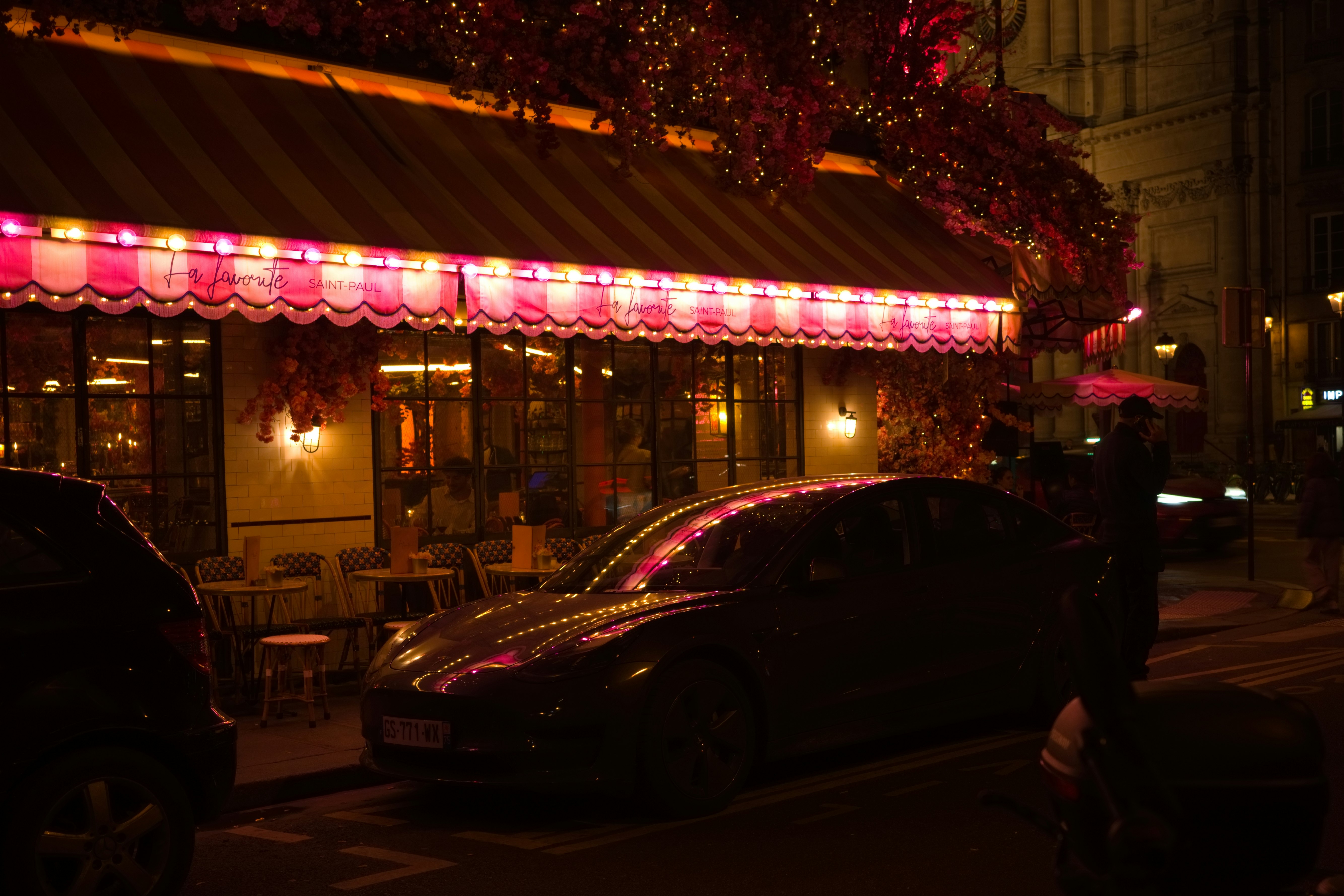 夜晚街角，燈火通明的咖啡館門前停著汽車