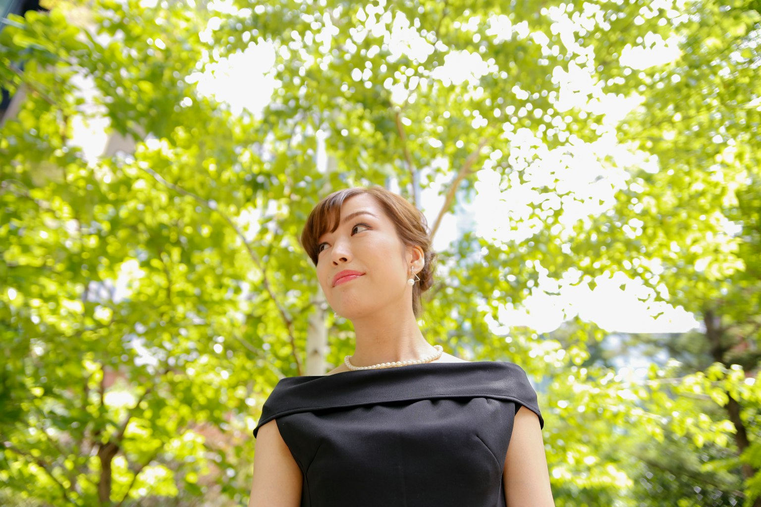 Une femme en robe noire regardant vers le haut sous des arbres verts