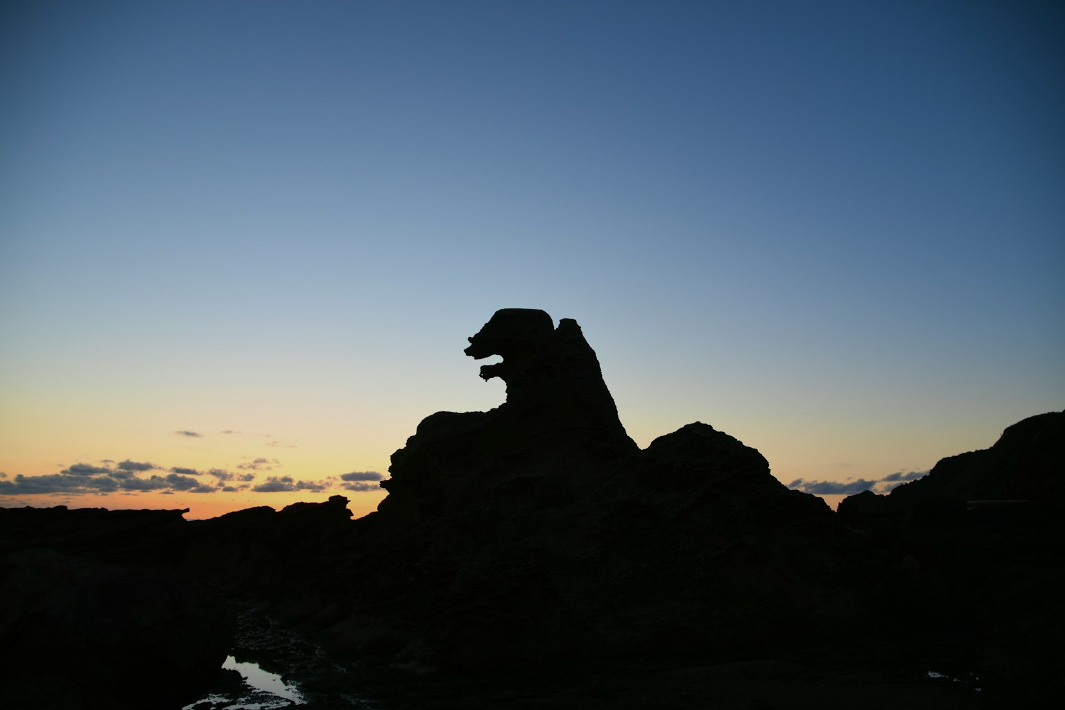 Silhouette einer Felsformation, die einem Wolf ähnelt, vor einem Sonnenuntergangshimmel