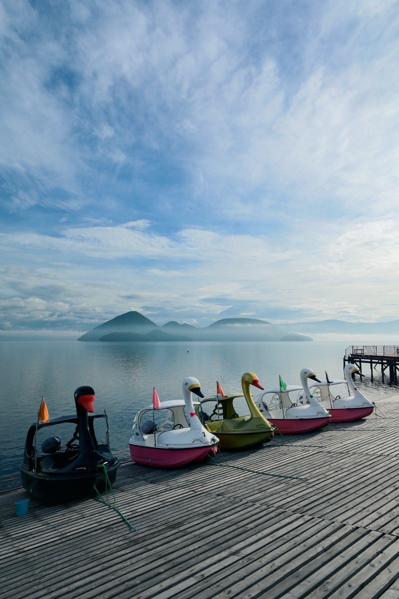 Perahu dayung berbentuk angsa berwarna-warni di tepi danau dengan air tenang