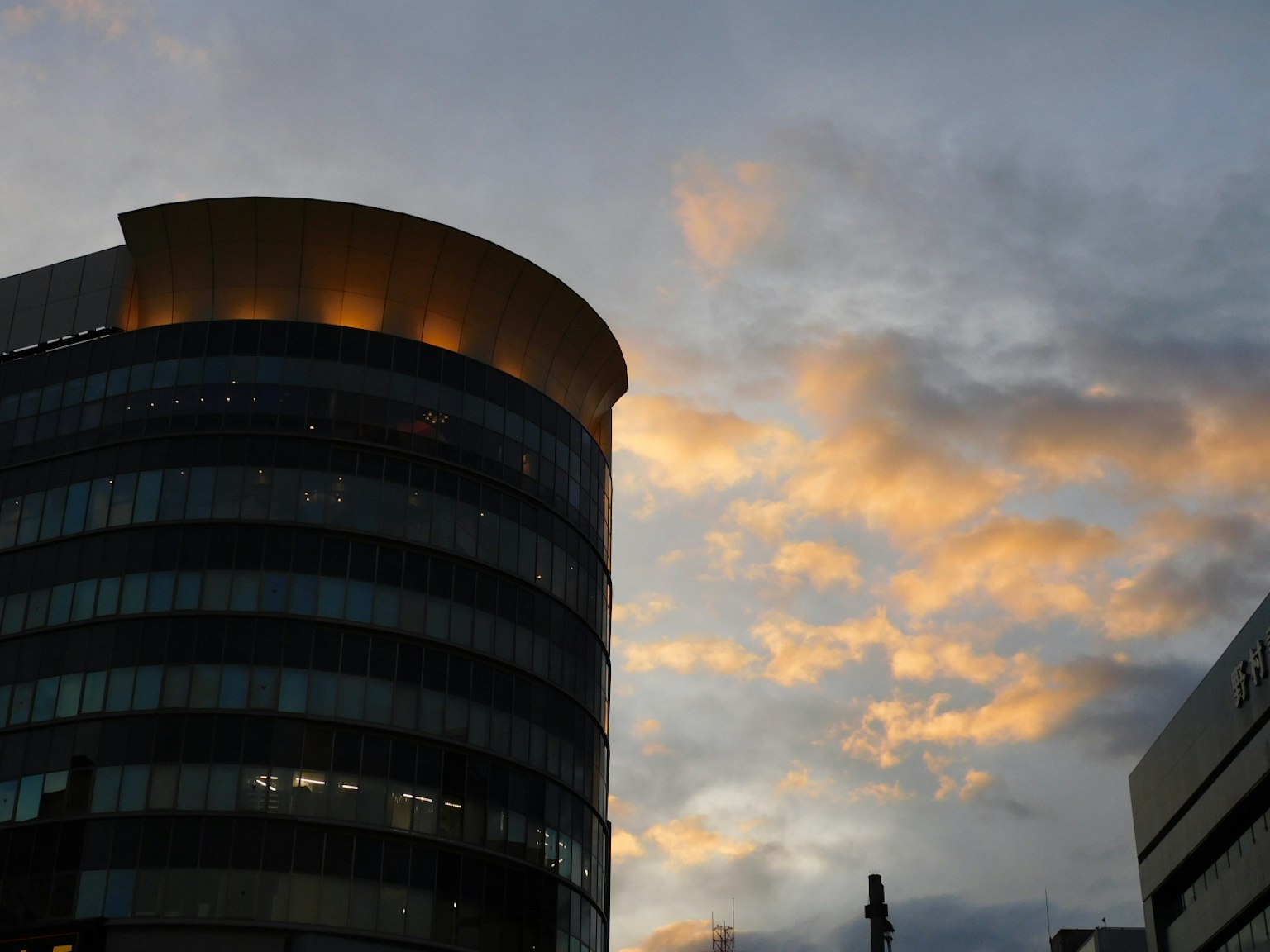 Façade d'un bâtiment moderne illuminée par le coucher de soleil avec un ciel nuageux