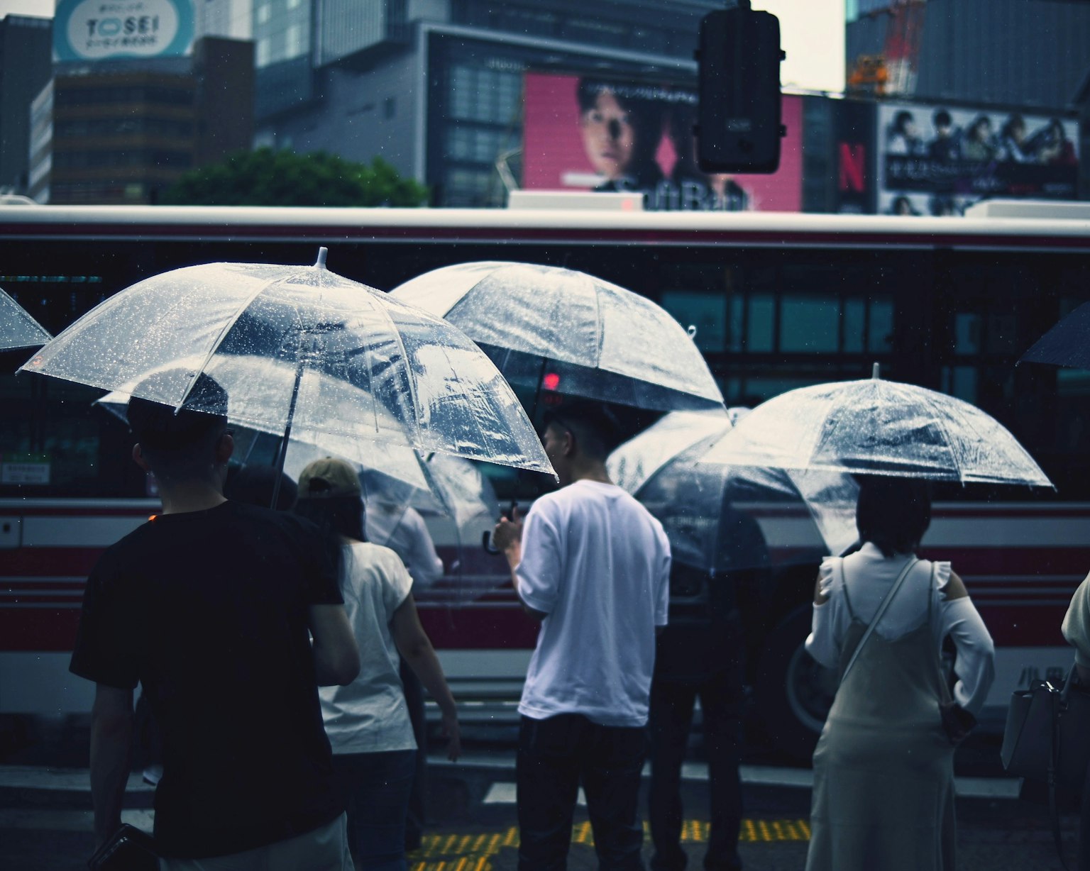 People holding umbrellas in the rain standing at a crosswalk with an urban backdrop