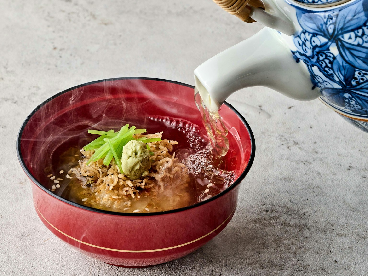 Soupe chaude versée dans un bol rouge avec du wasabi et une garniture verte