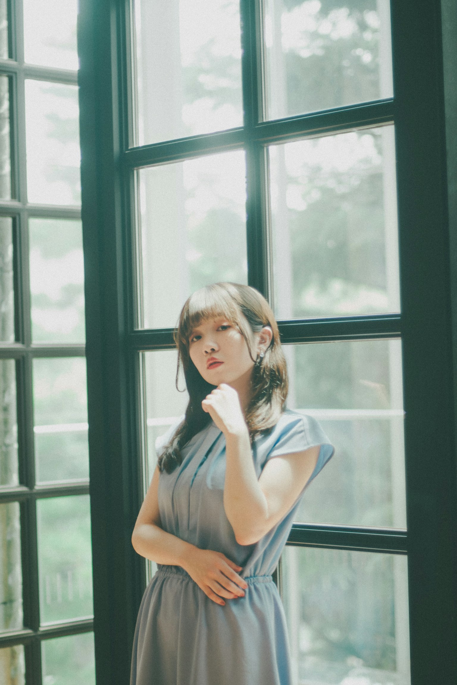 窗边站着的女性肖像 穿着蓝色裙子 面带平静的表情和姿势