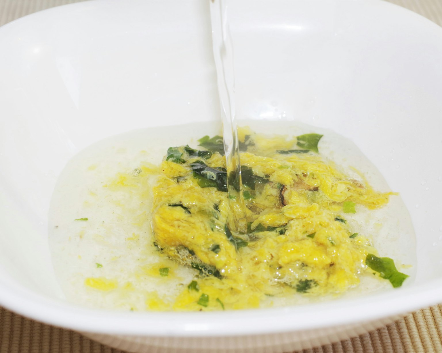 A white bowl filled with a soup-like dish containing eggs and greens