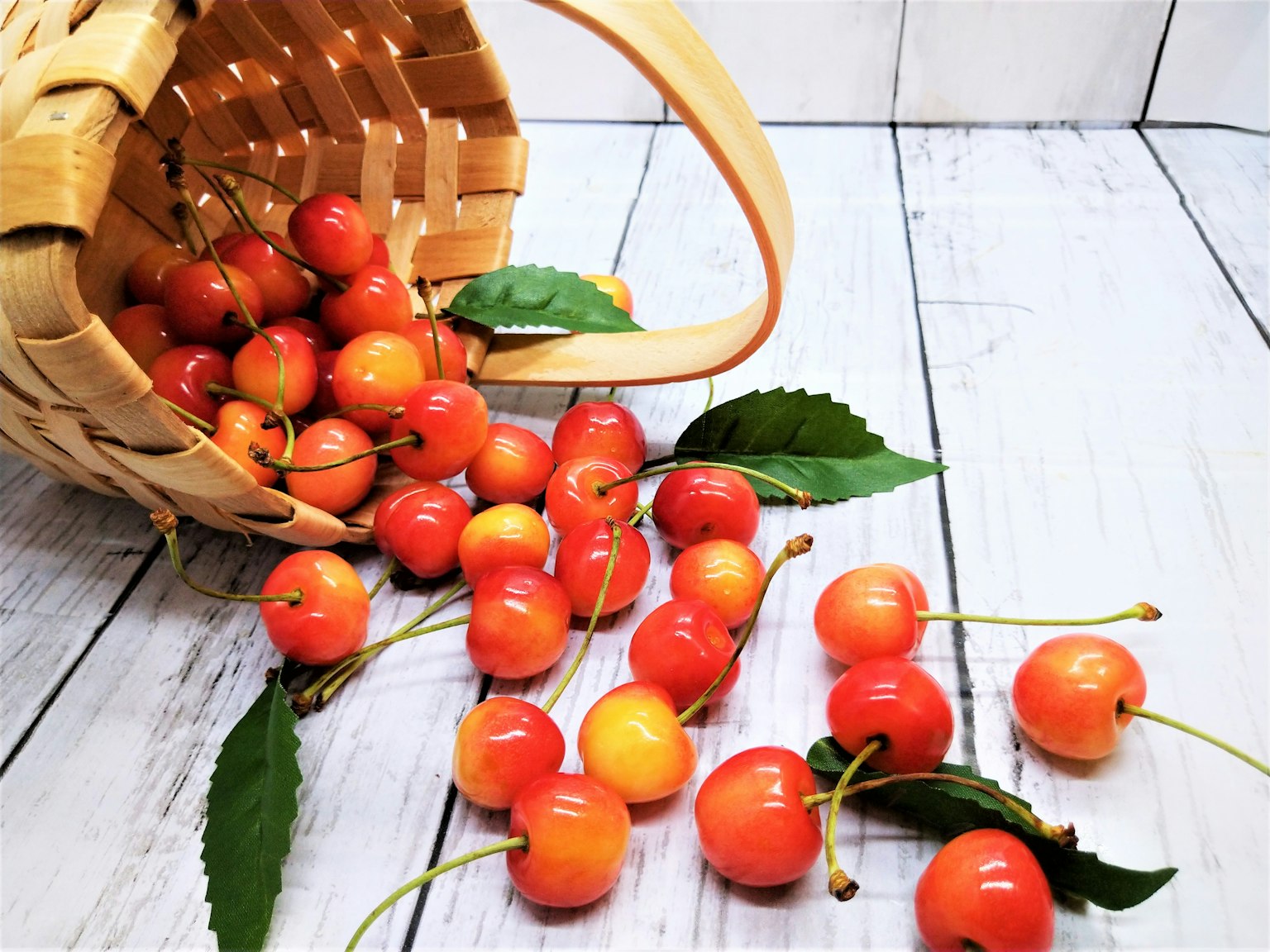 Cerezas rojas y naranjas derramándose de una canasta de mimbre con hojas verdes