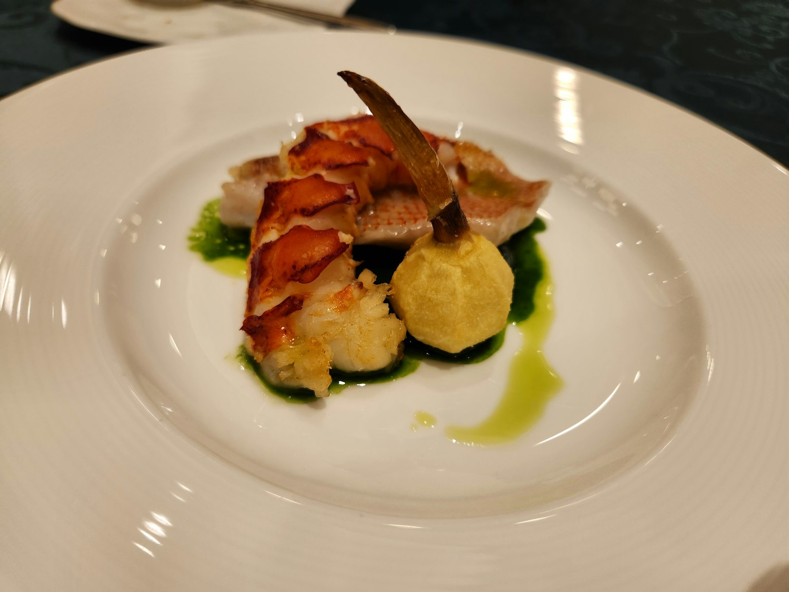 A beautifully plated dish featuring lobster with a ball of mashed potato on a bed of green sauce