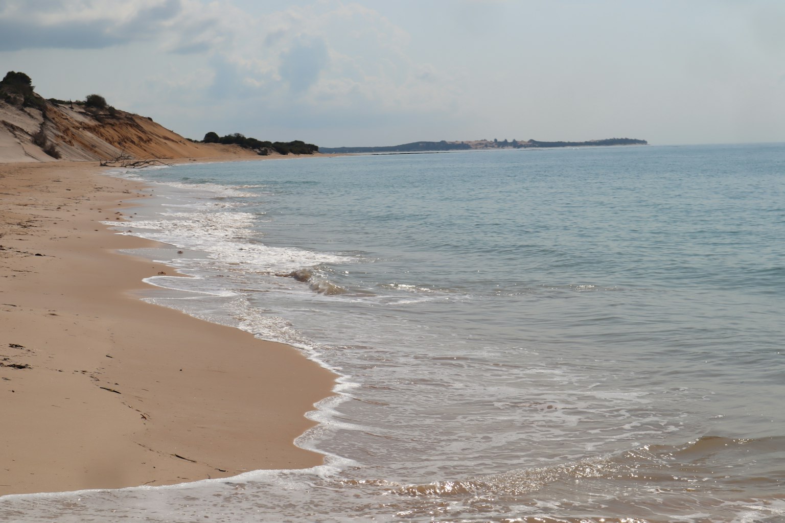 Pemandangan pantai yang tenang ombak lembut menyapu pasir