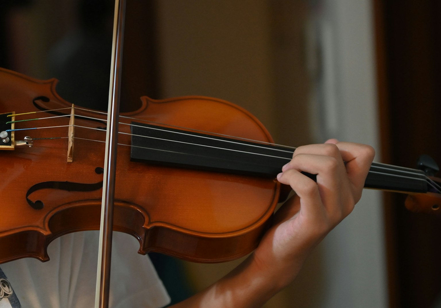 Kedekatan tangan yang memainkan biola menampilkan serat kayu yang indah dari alat musik