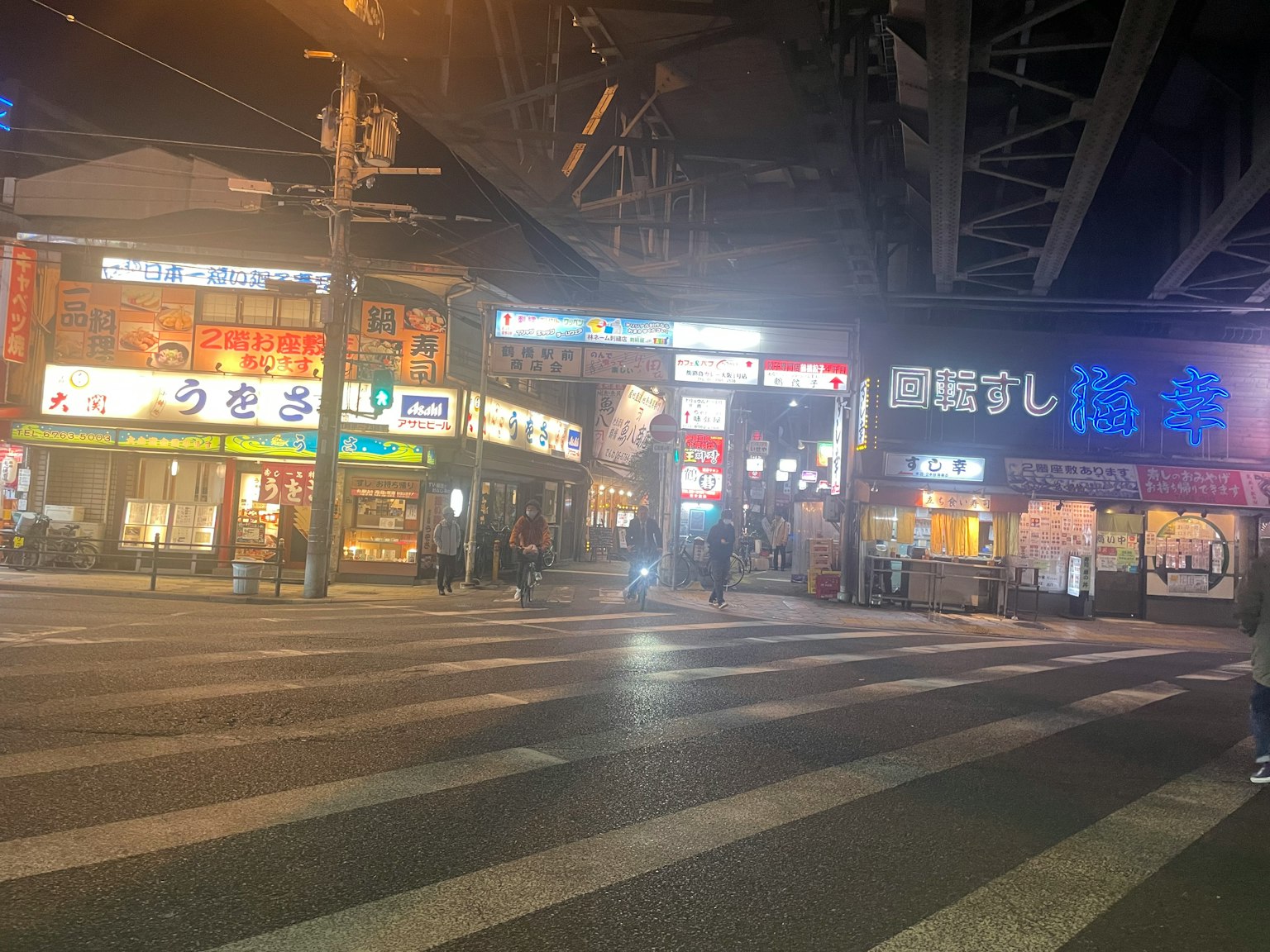 Nächtliche Szene einer belebten Straße mit Restaurantschildern und Zebrastreifen