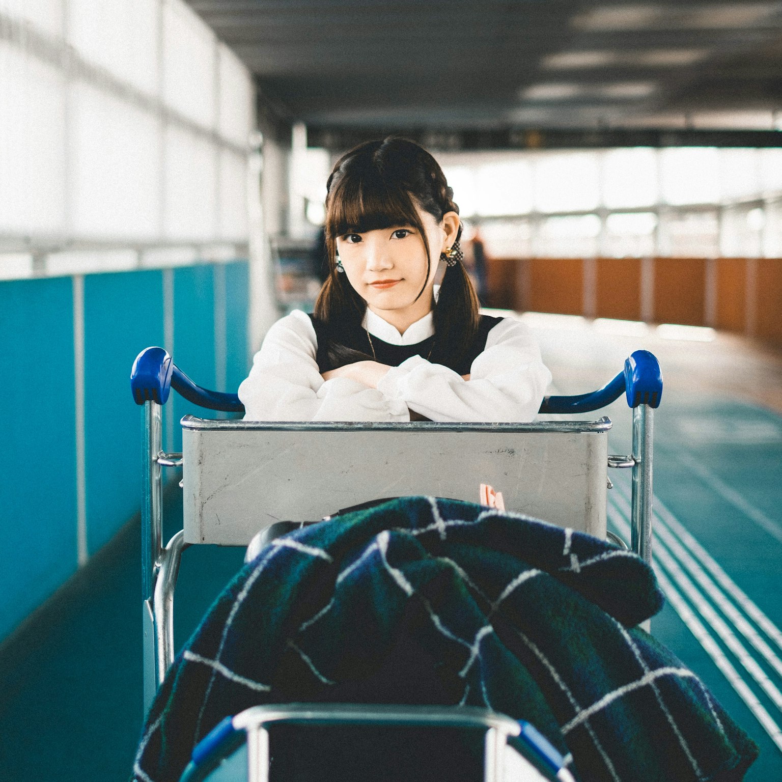 Mädchen, das auf einem Flughafenwagen sitzt, mit schwarzen Haaren, trägt eine weiße Bluse und eine schwarze Weste