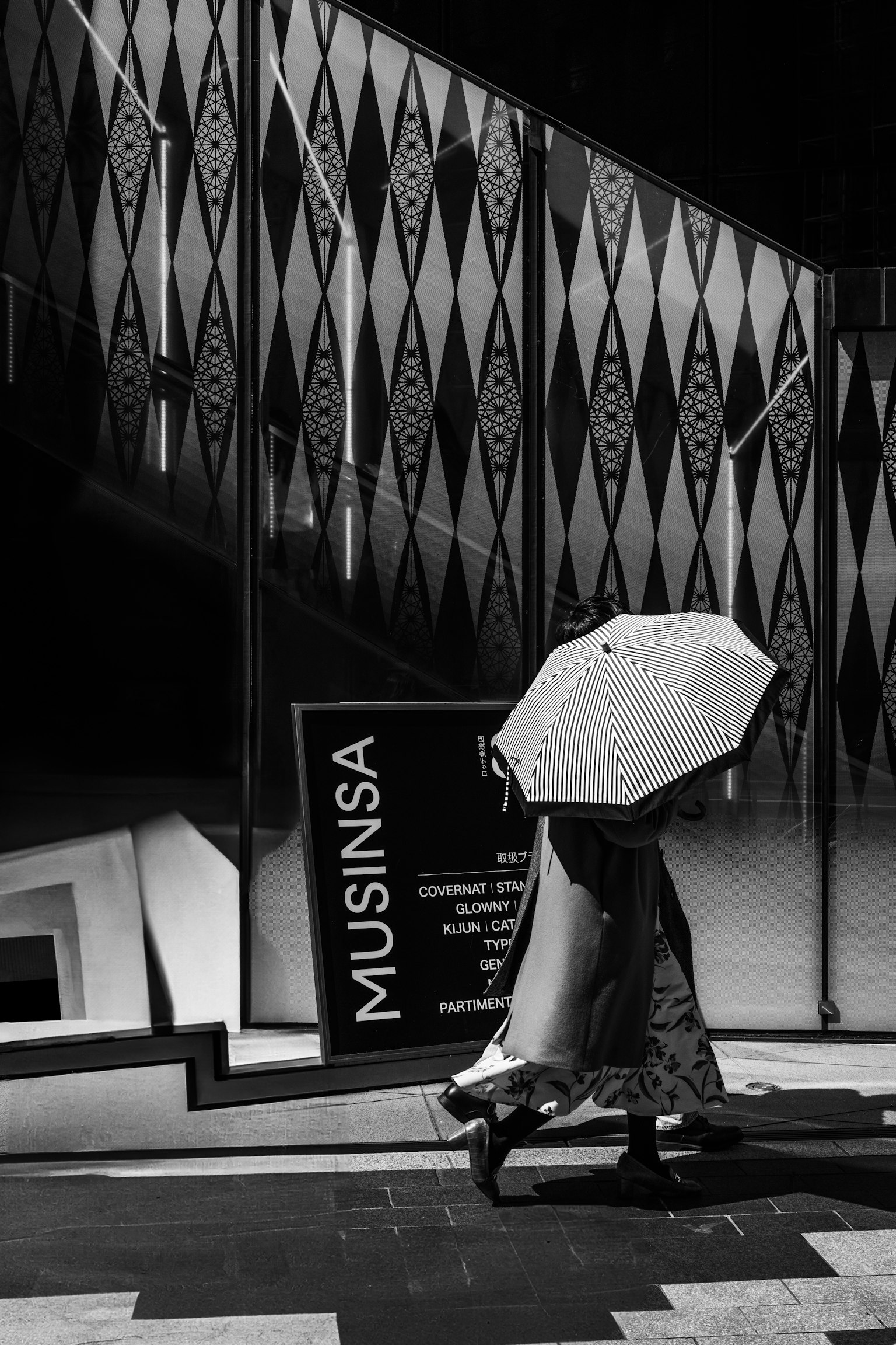 一位手持雨伞的人在MUSINSA标志前走,黑白照片