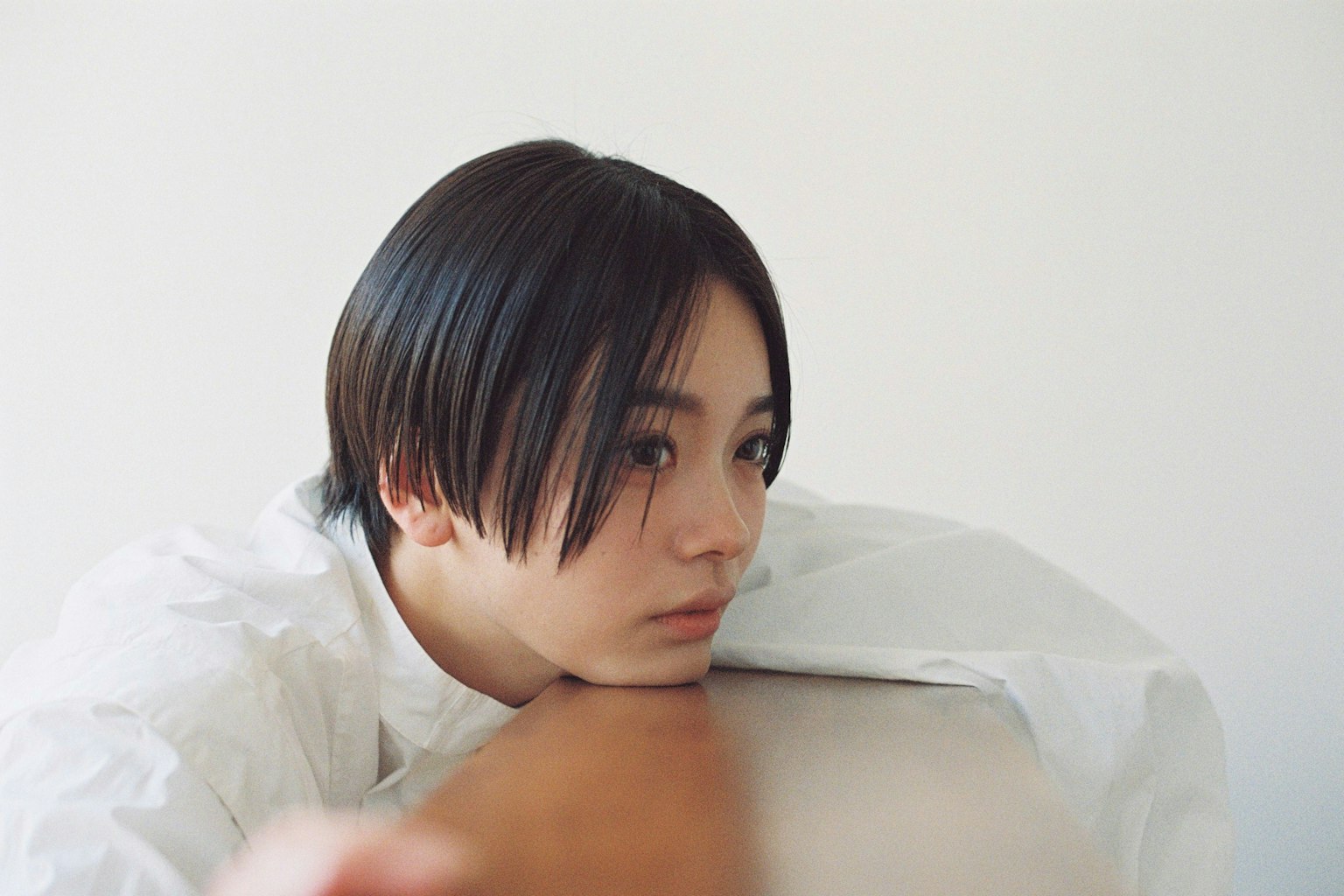 Portrait of a short-haired woman resting against a surface with a white background