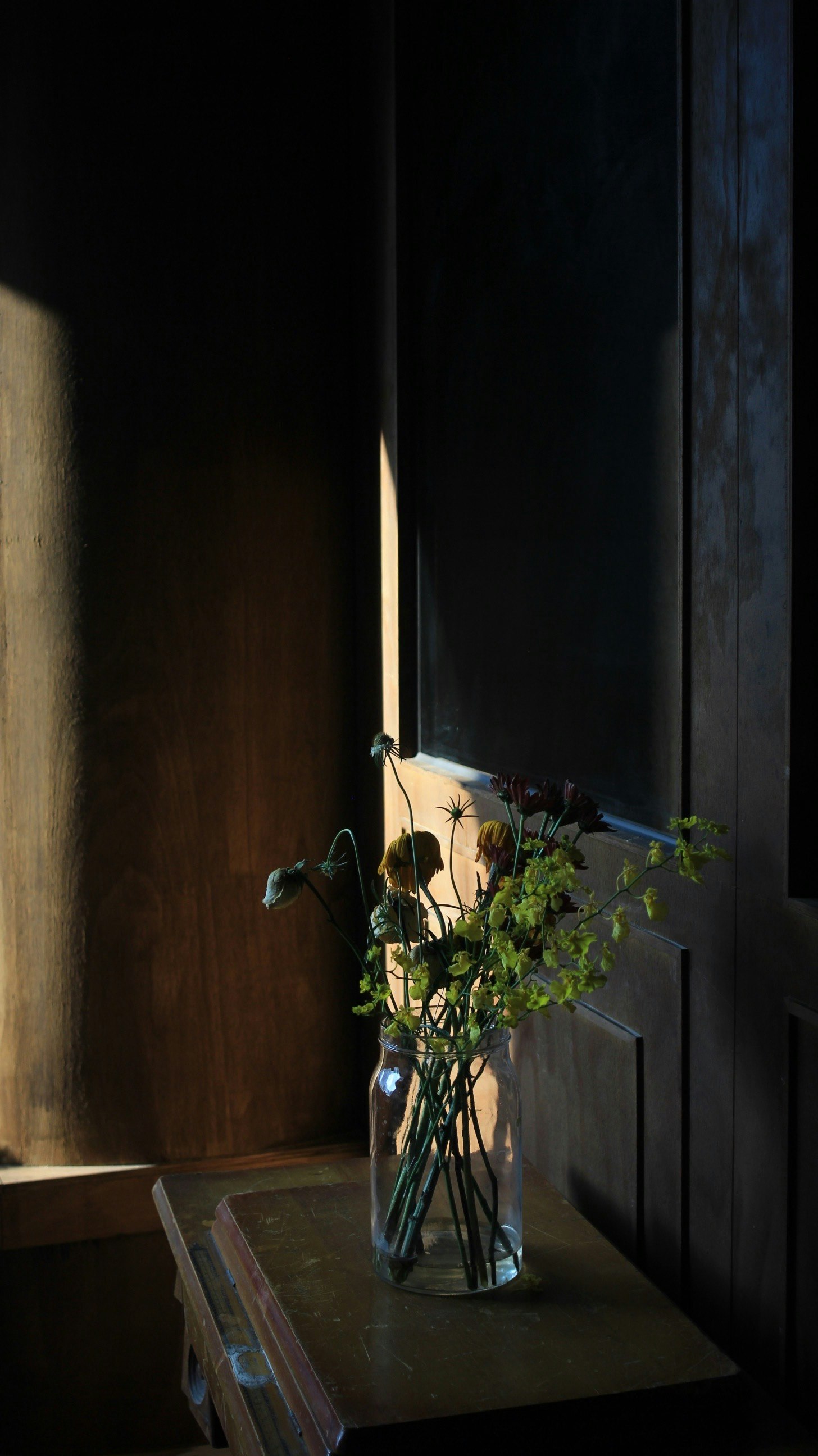 木製の壁と扉のある室内の窓辺に置かれた花の花瓶