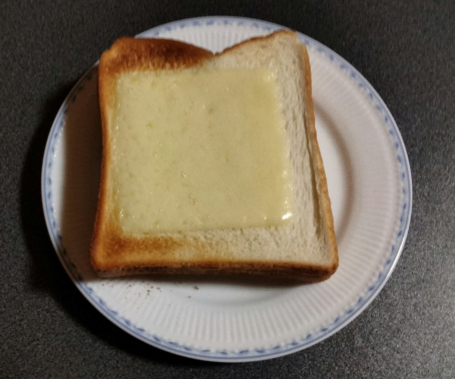 Một lát bánh mì nướng được phủ bơ chảy trên đĩa trắng