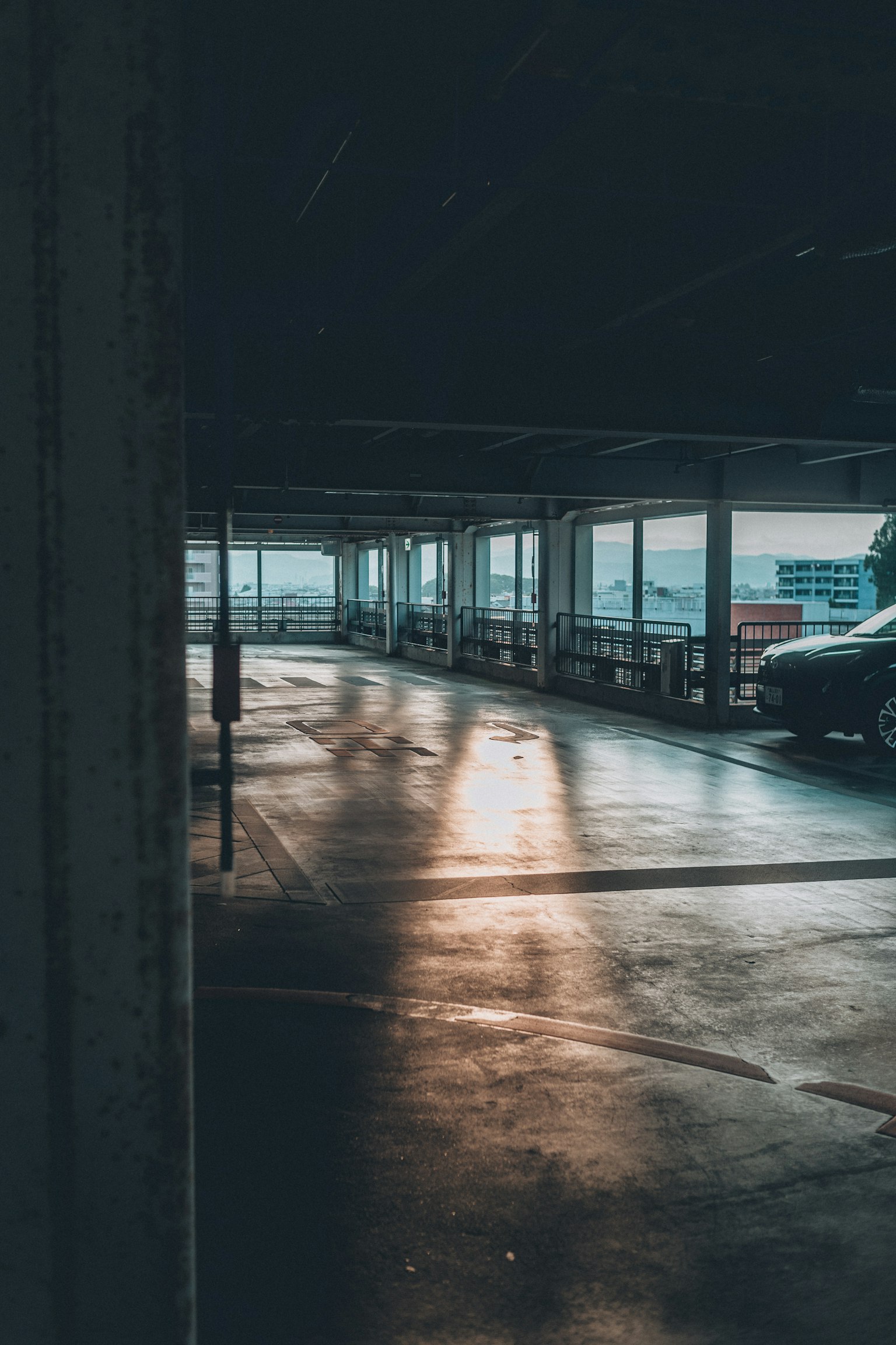 昏暗的停車場內，陽光在一輛車旁的地面上反射