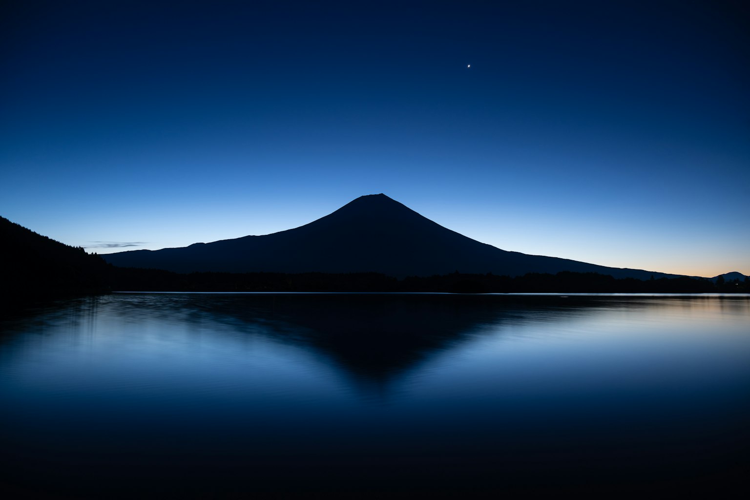 Silhouette of Mount Fuji at night with reflection on water