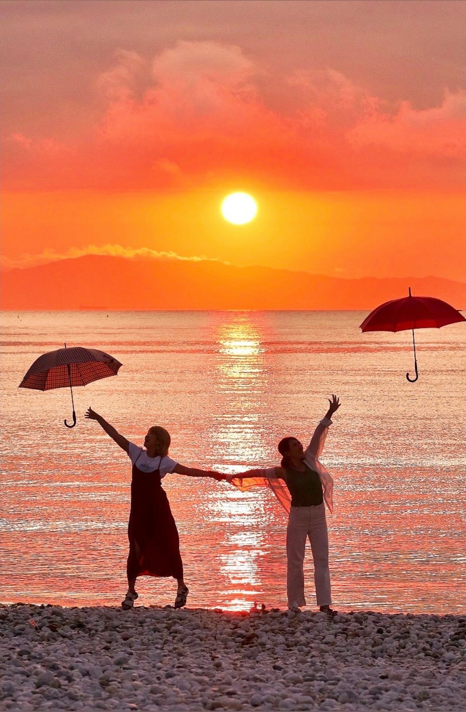 Deux personnes tenant des parapluies rouges se tenant sur une plage au coucher du soleil
