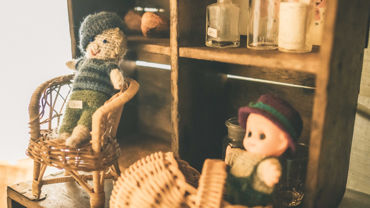 Charming dolls in wicker chairs with a cozy shelf background