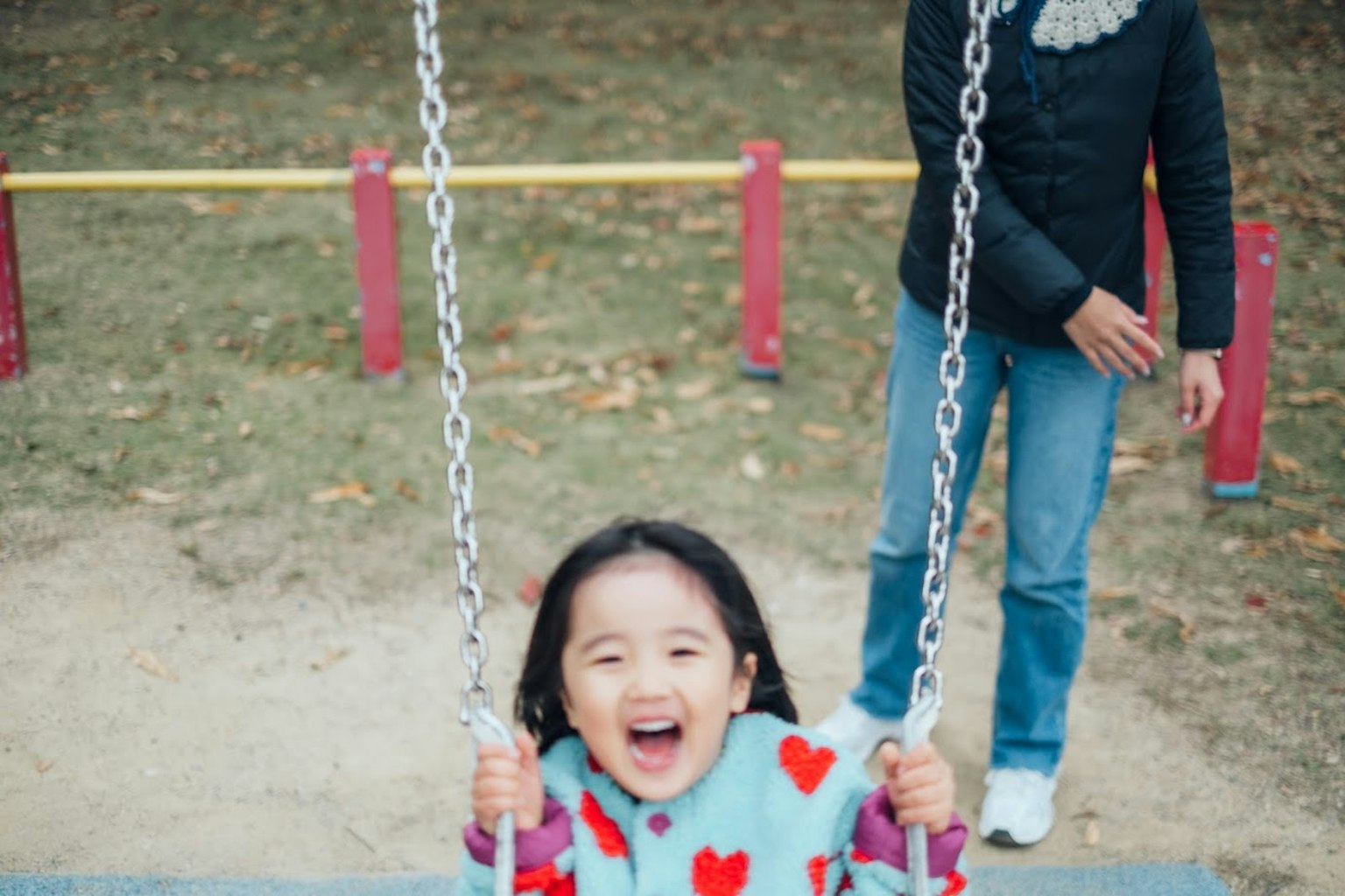 Smiling girl on a swing in a park with an adult in the background