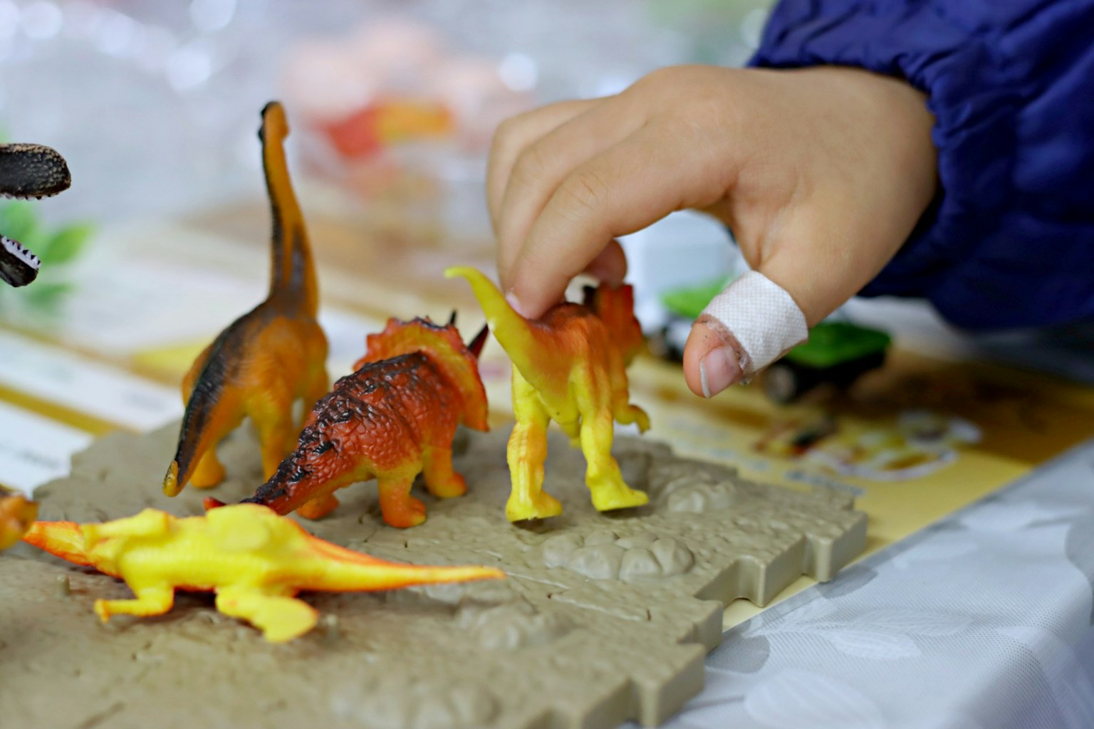 A child's hand interacting with colorful dinosaur toys on a play surface