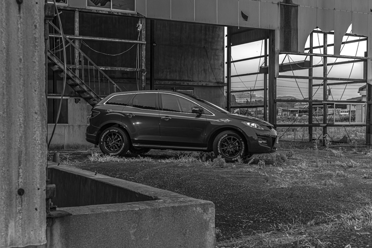 Un coche negro estacionado en un área deteriorada con estructuras metálicas