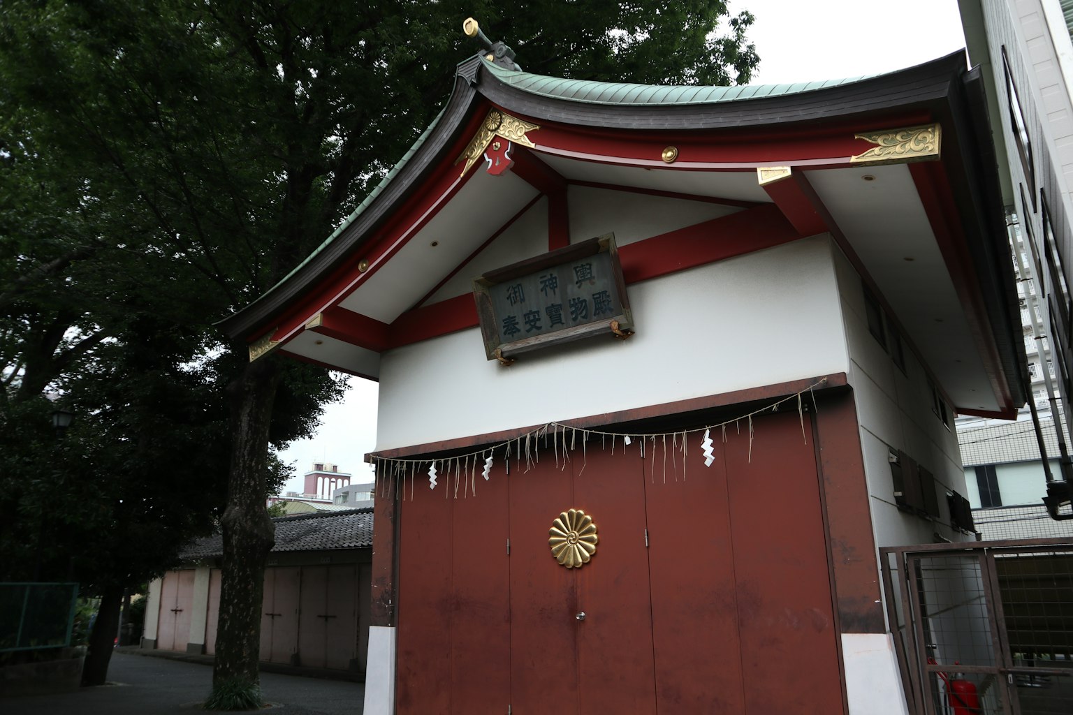 Extérieur d'un bâtiment japonais traditionnel avec un toit rouge et des murs blancs, avec un symbole doré au centre entouré d'arbres verts