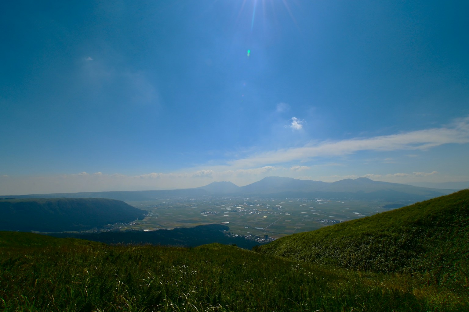 Vaste colline verde sotto un cielo blu con montagne lontane