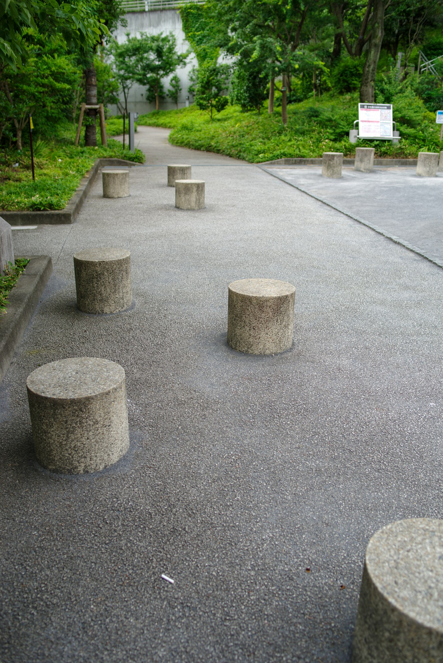 Concrete cylindrical stools arranged along a paved path surrounded by greenery