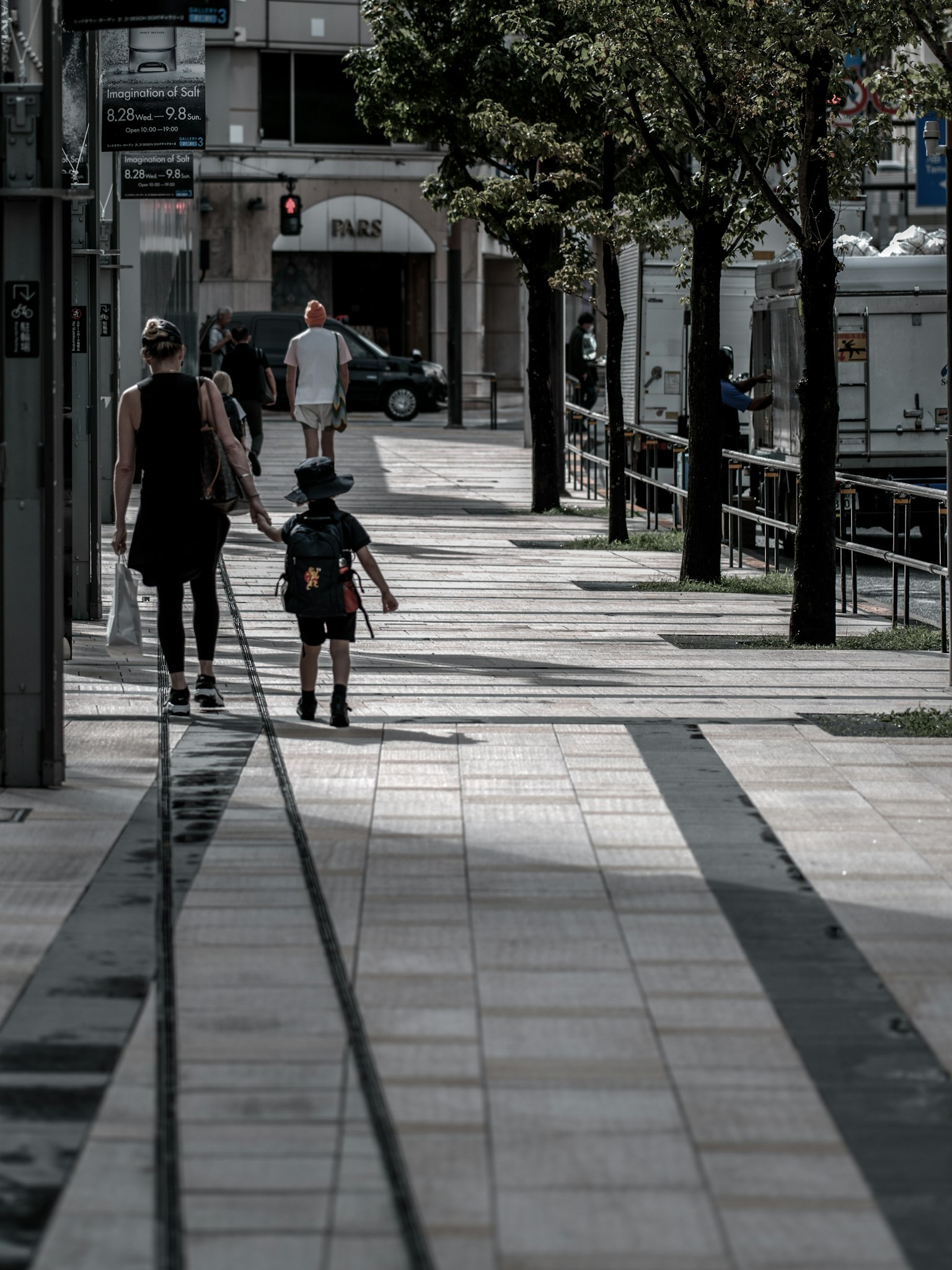 Un genitore e un bambino che camminano su un marciapiede cittadino con alberi e lampioni