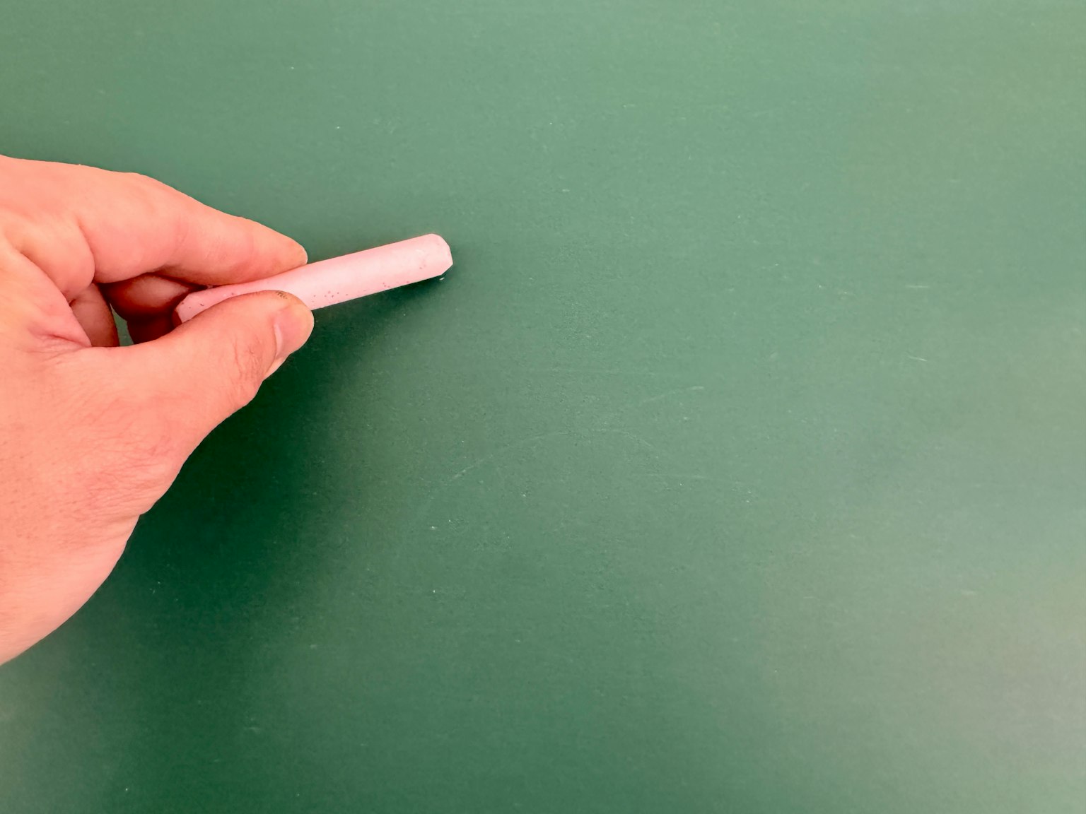 Sebuah tangan memegang kapur putih menyentuh papan tulis hijau