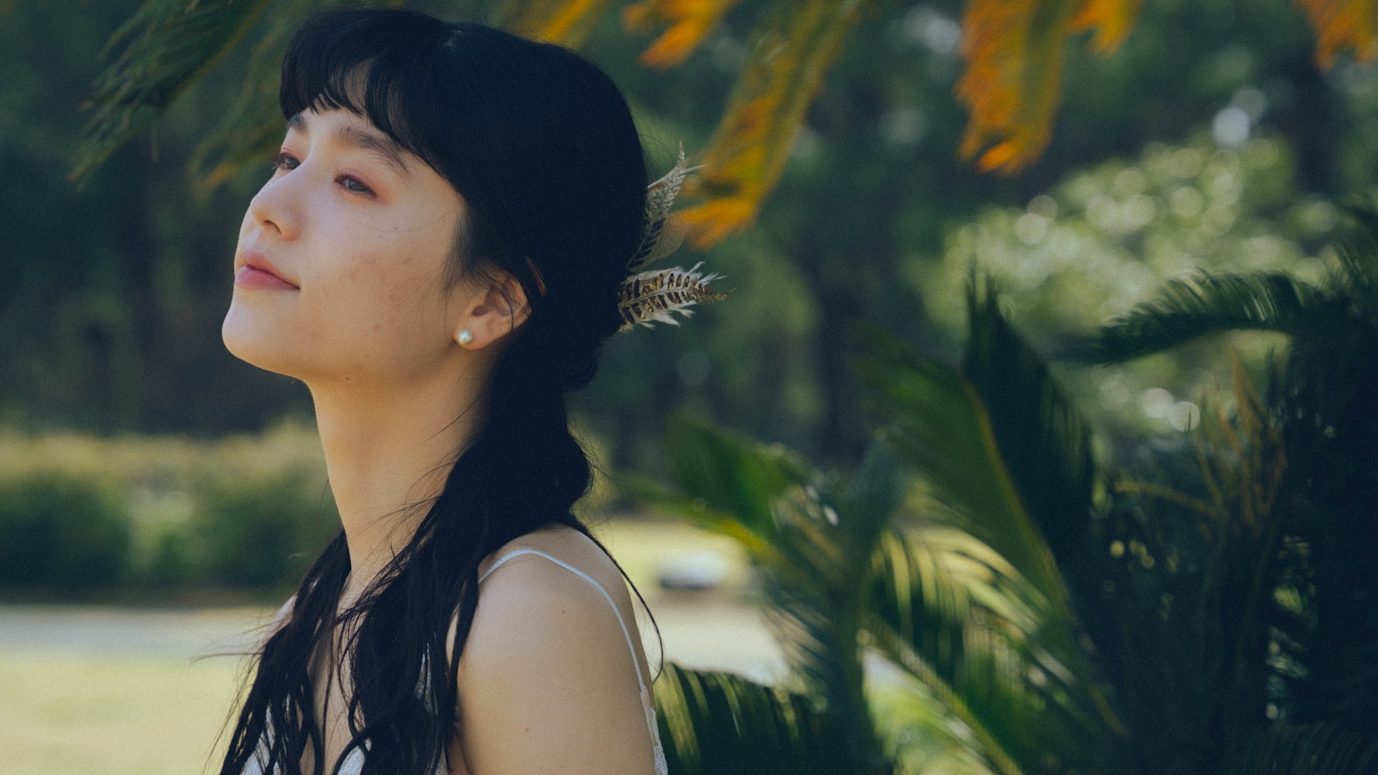 Seitenansicht einer lächelnden Frau in der Natur mit einem blumigen Haarschmuck und grünem Hintergrund