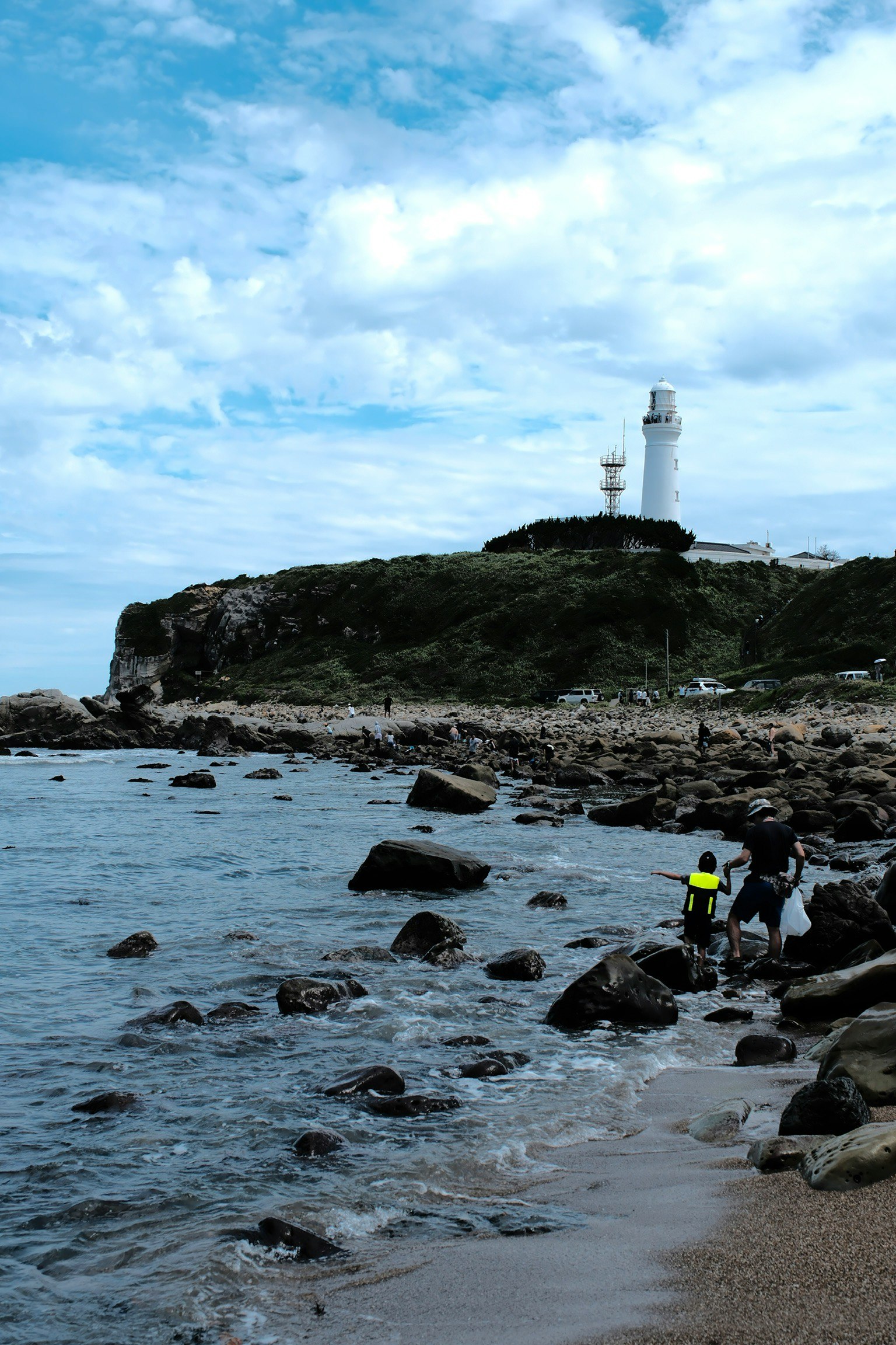海岸の岩場で作業する人と灯台の風景