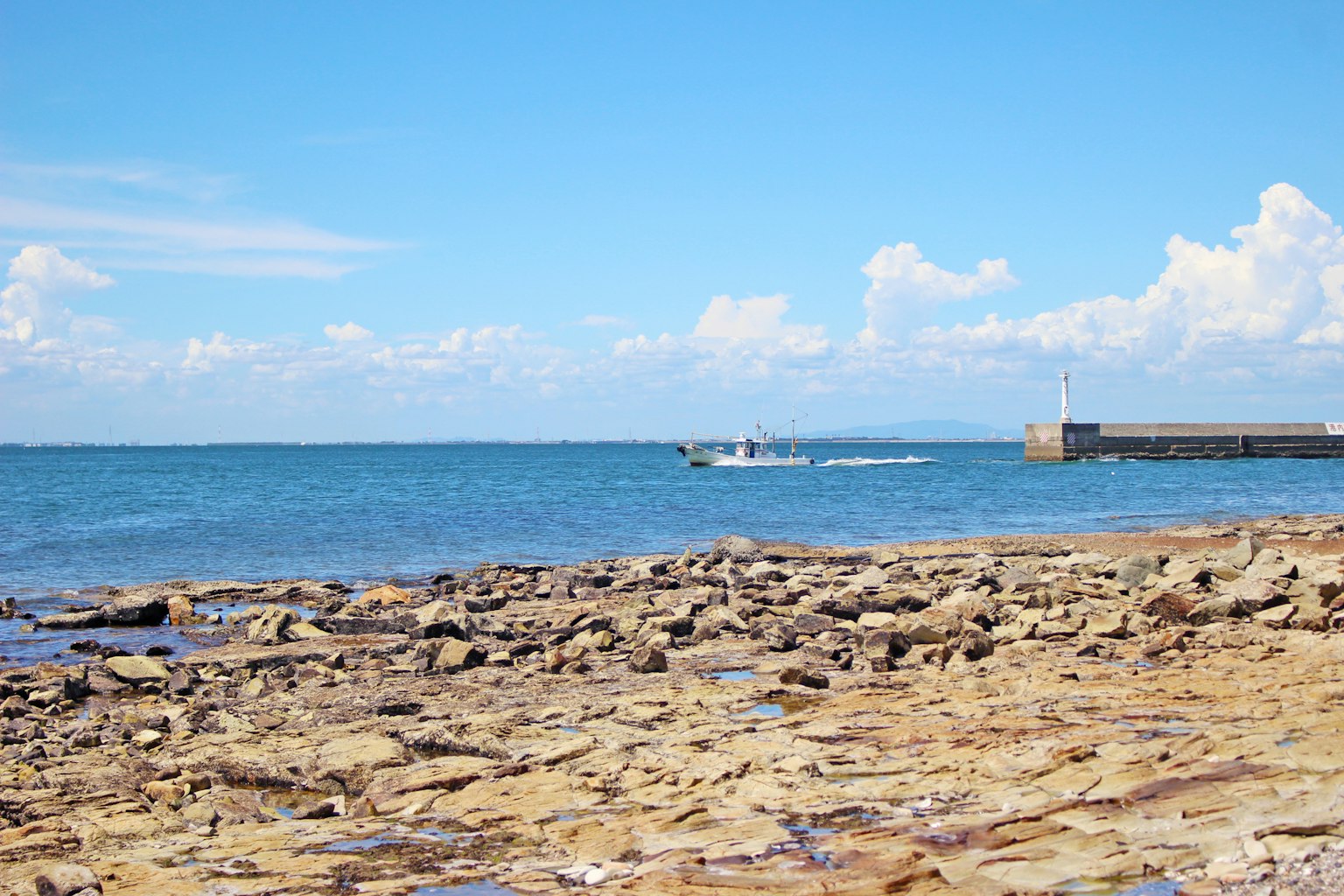 Malersicher Blick auf den blauen Ozean und den felsigen Strand mit einem Boot in der Ferne
